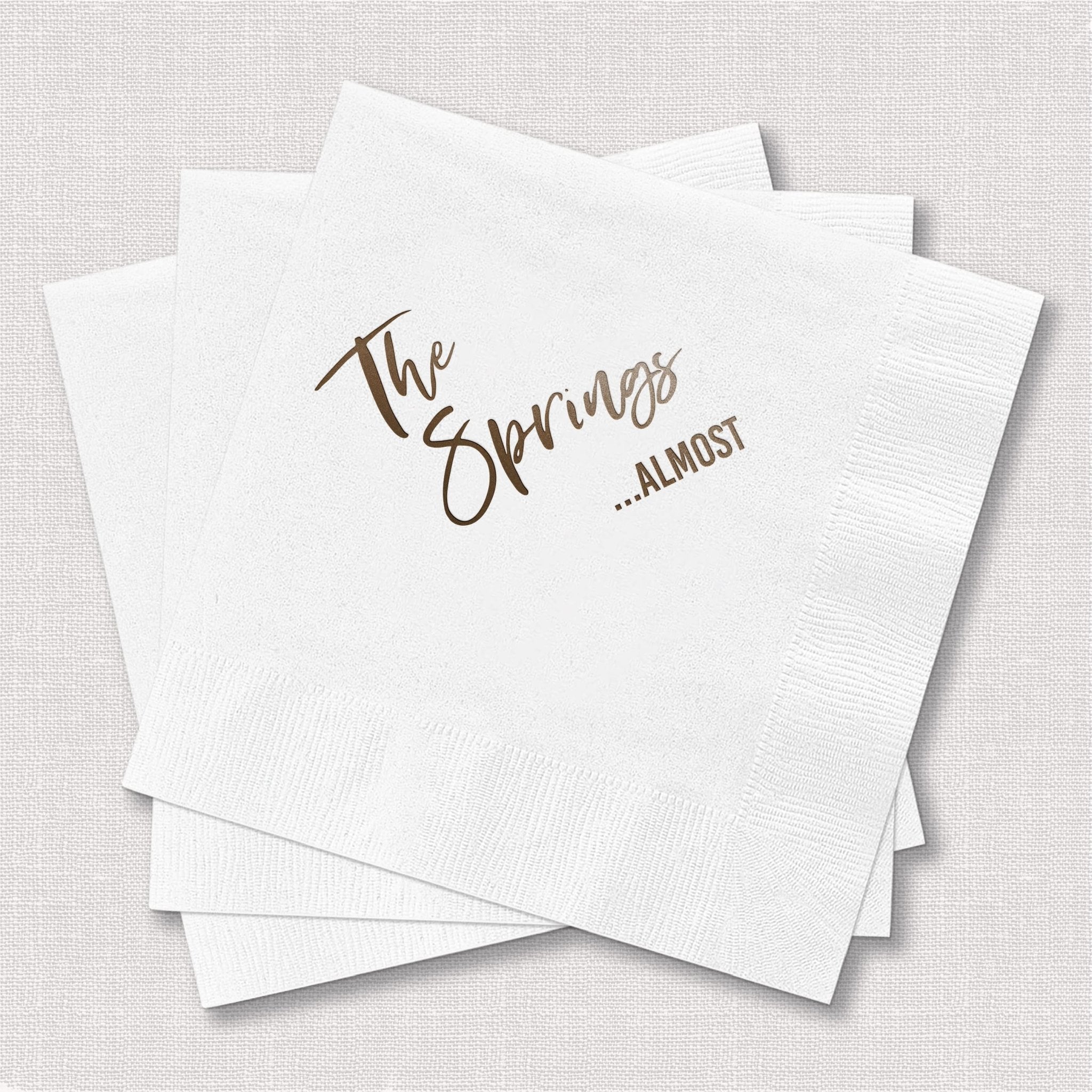 White cocktail napkins with gold foil text reading "The Openings ...Almost"