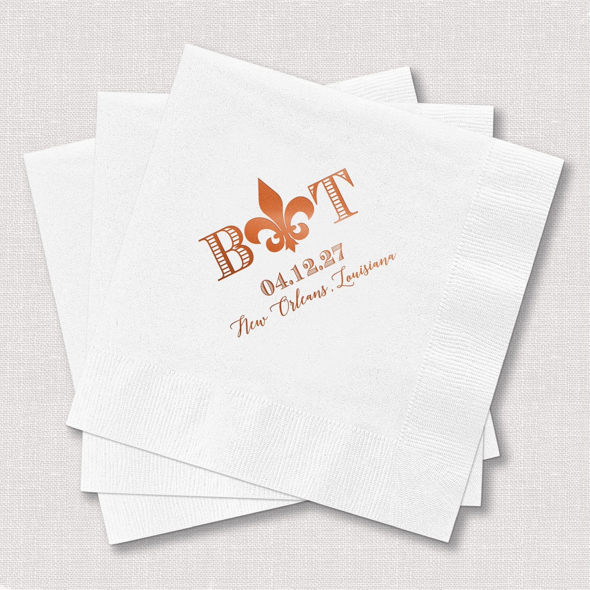 White cocktail napkins with copper foil stamped Fleur De Lis design and "Boast" text with personalized wedding date and location details.