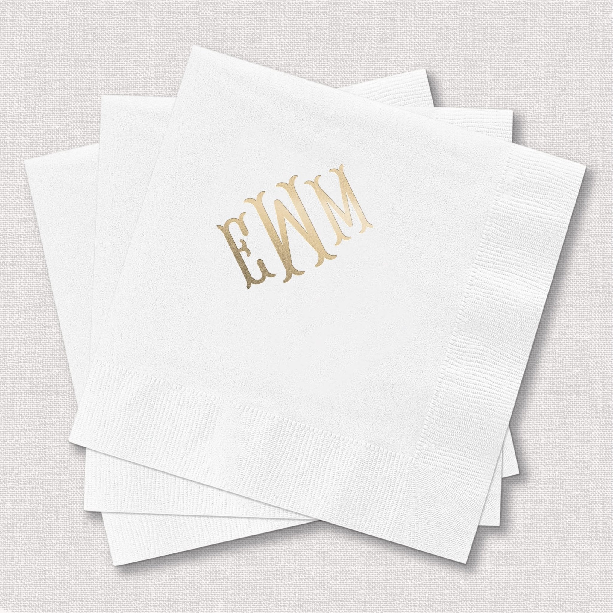 Stack of white cocktail napkins with gold foil monogram "EKNN" printed on corner