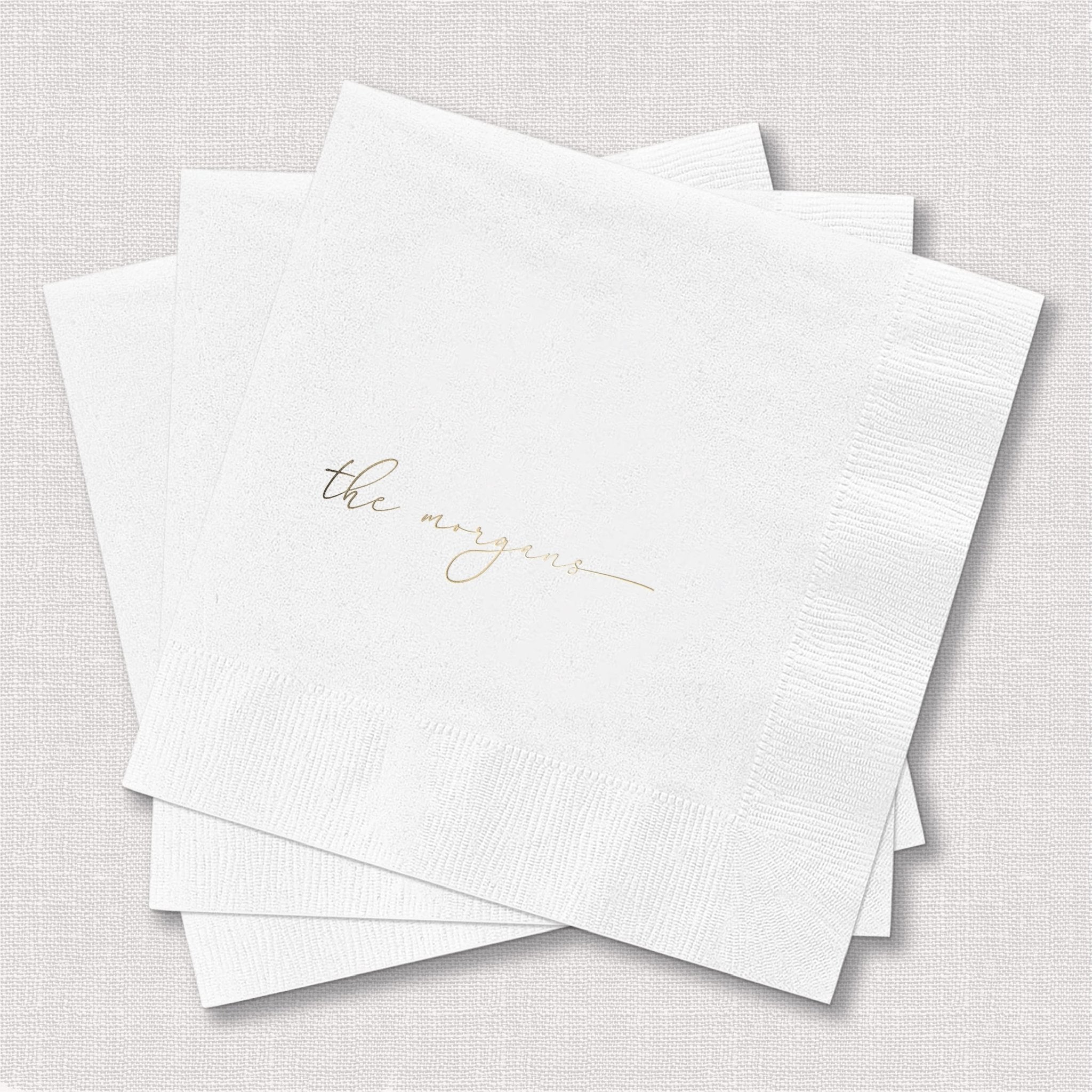 Stack of white cocktail napkins with gold foil stamped script text reading "the newlyweds"