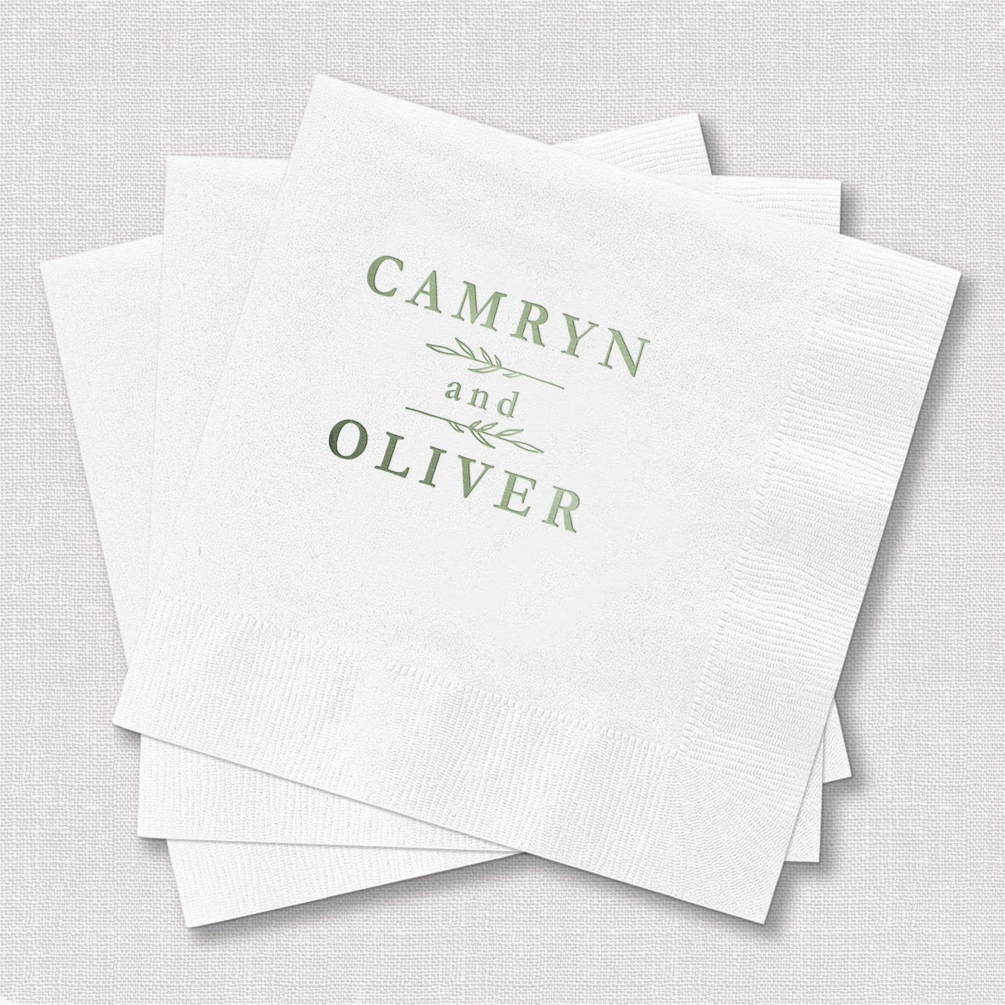 White napkins with sage green foil-stamped text reading "CAMRYN and OLIVER" with decorative line accents