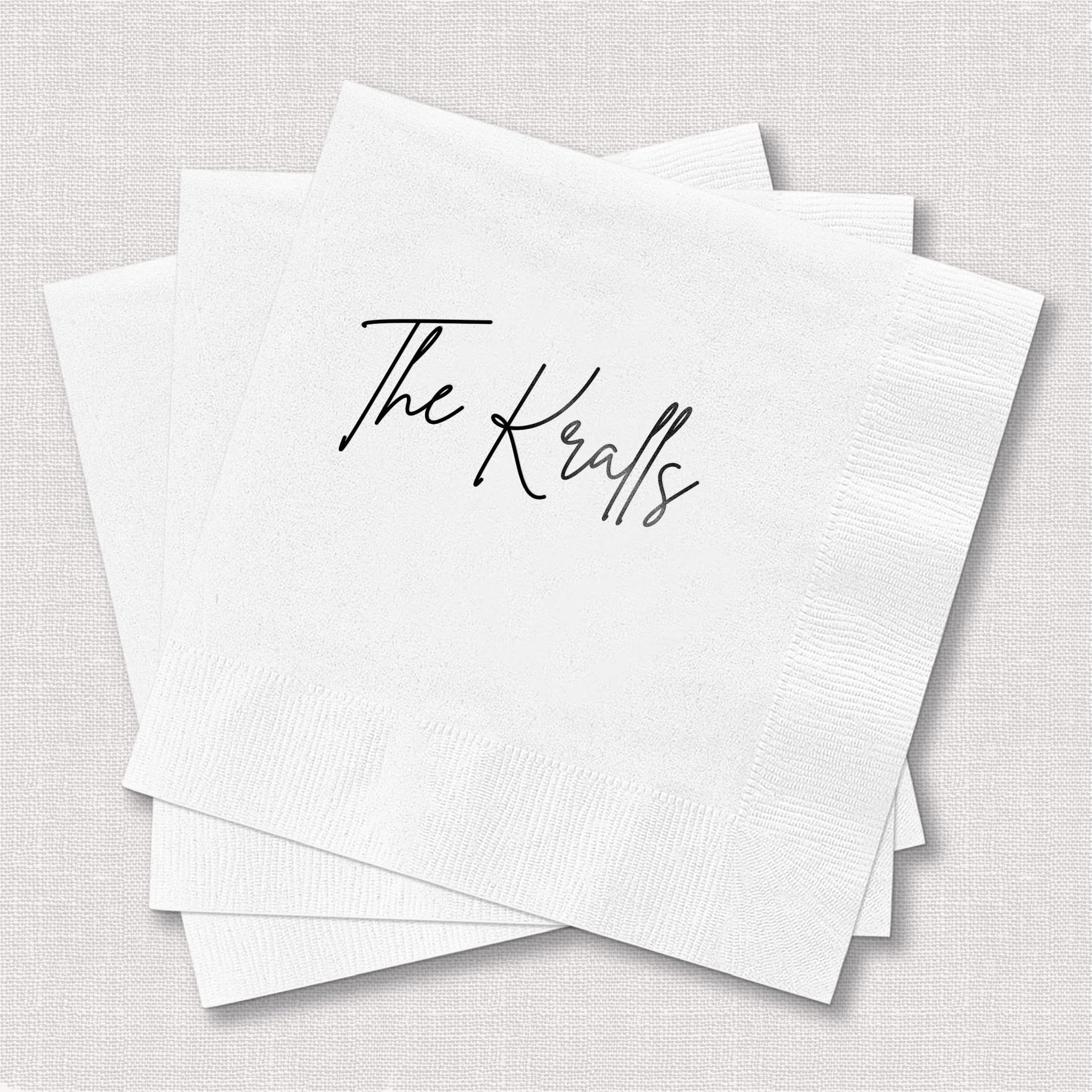 White cocktail napkins with "The Kraals" in black script lettering, stack of personalized wedding napkins