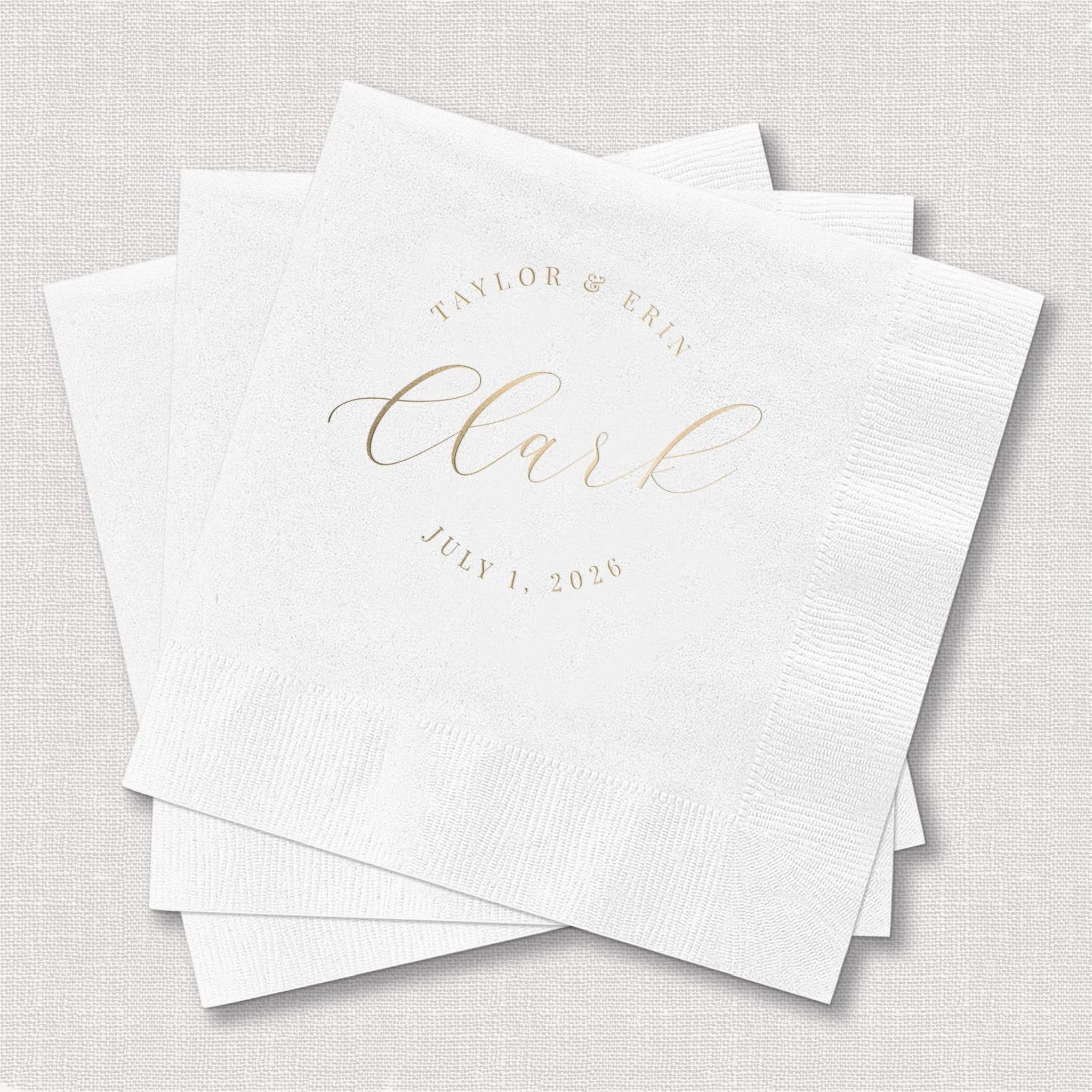 Stack of white cocktail napkins with gold foil stamped text reading "Taylor & Erin" and "Cheers" with wedding date July 1, 2025.