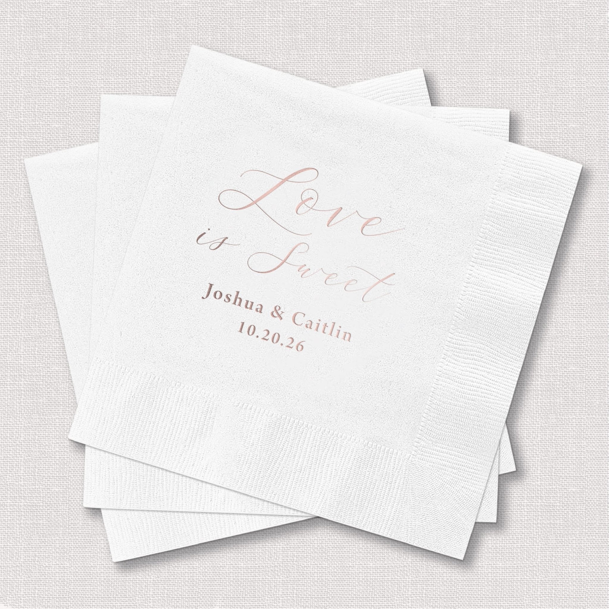 White cocktail napkins with rose gold foil stamped "Love is Sweet" text and personalized couple names and wedding date.