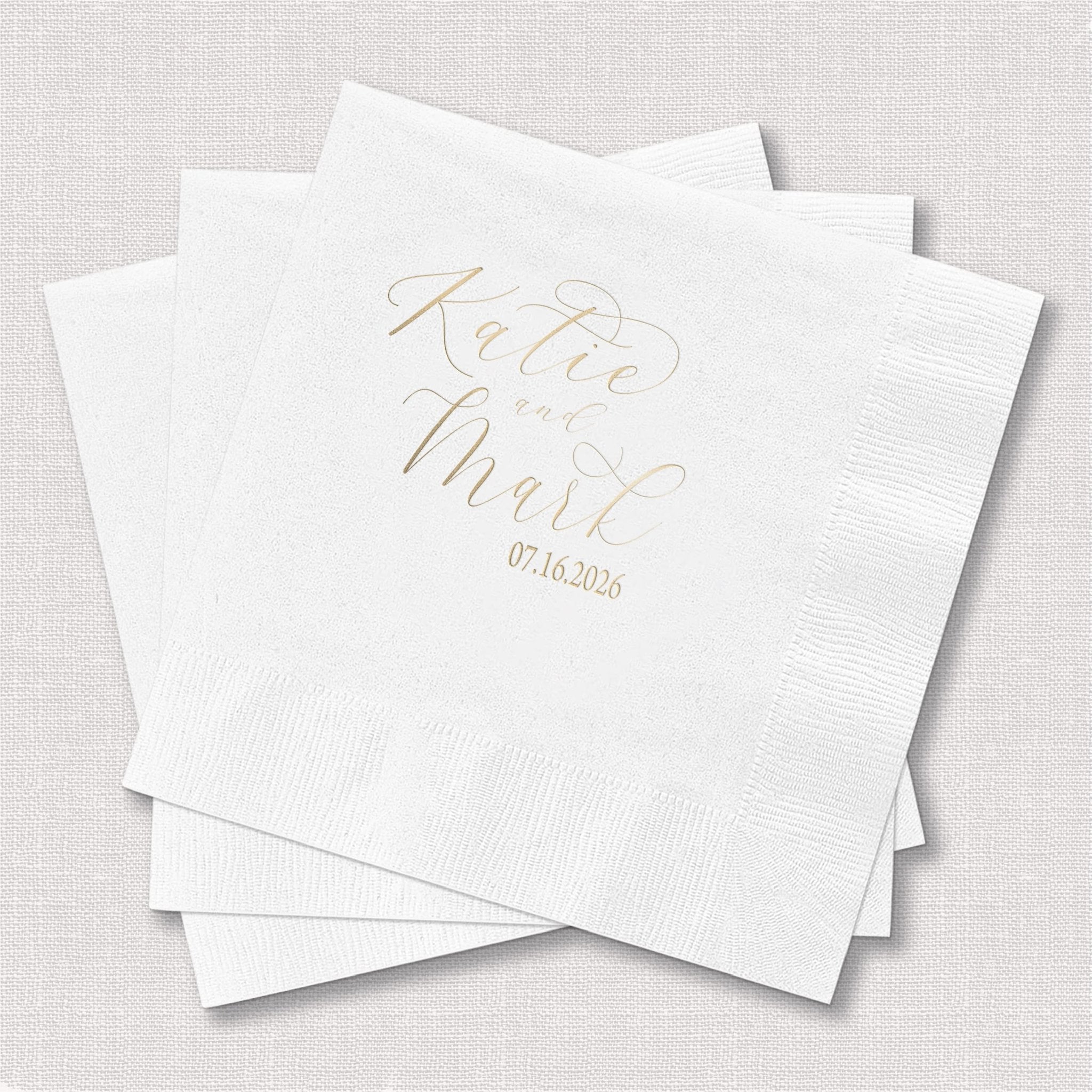 White cocktail napkins with gold foil stamped text reading "Kate and Mark" and wedding date 07.16.2022
