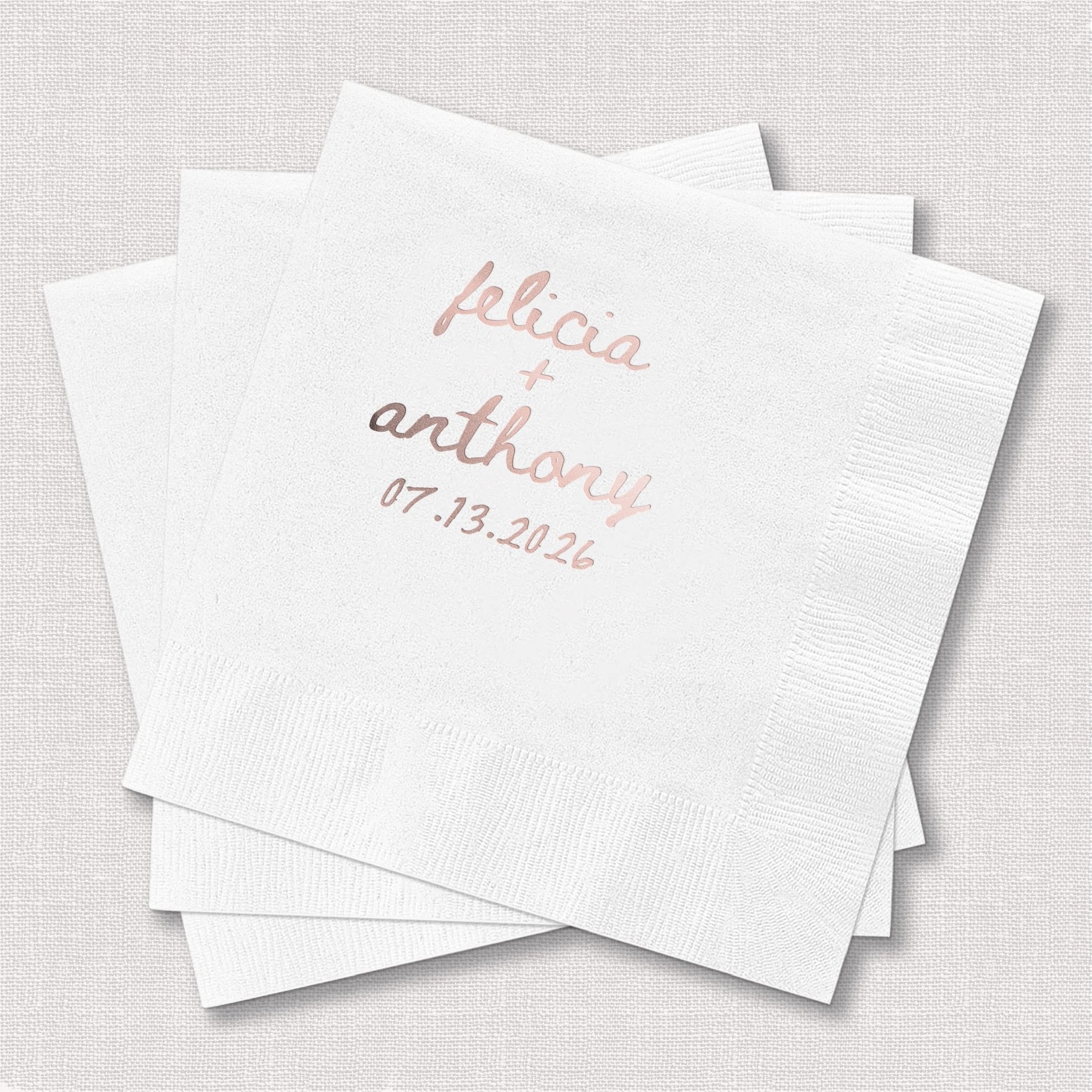 White cocktail napkins with "felicia" in pink foil and "anthony" with date in gold foil personalization.
