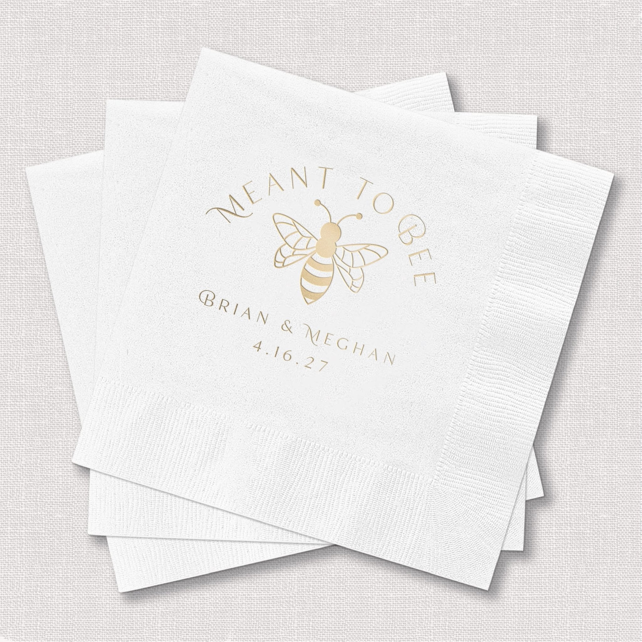 White cocktail napkins with gold foil bee design and "Meant to Bee" text with couple names and wedding date
