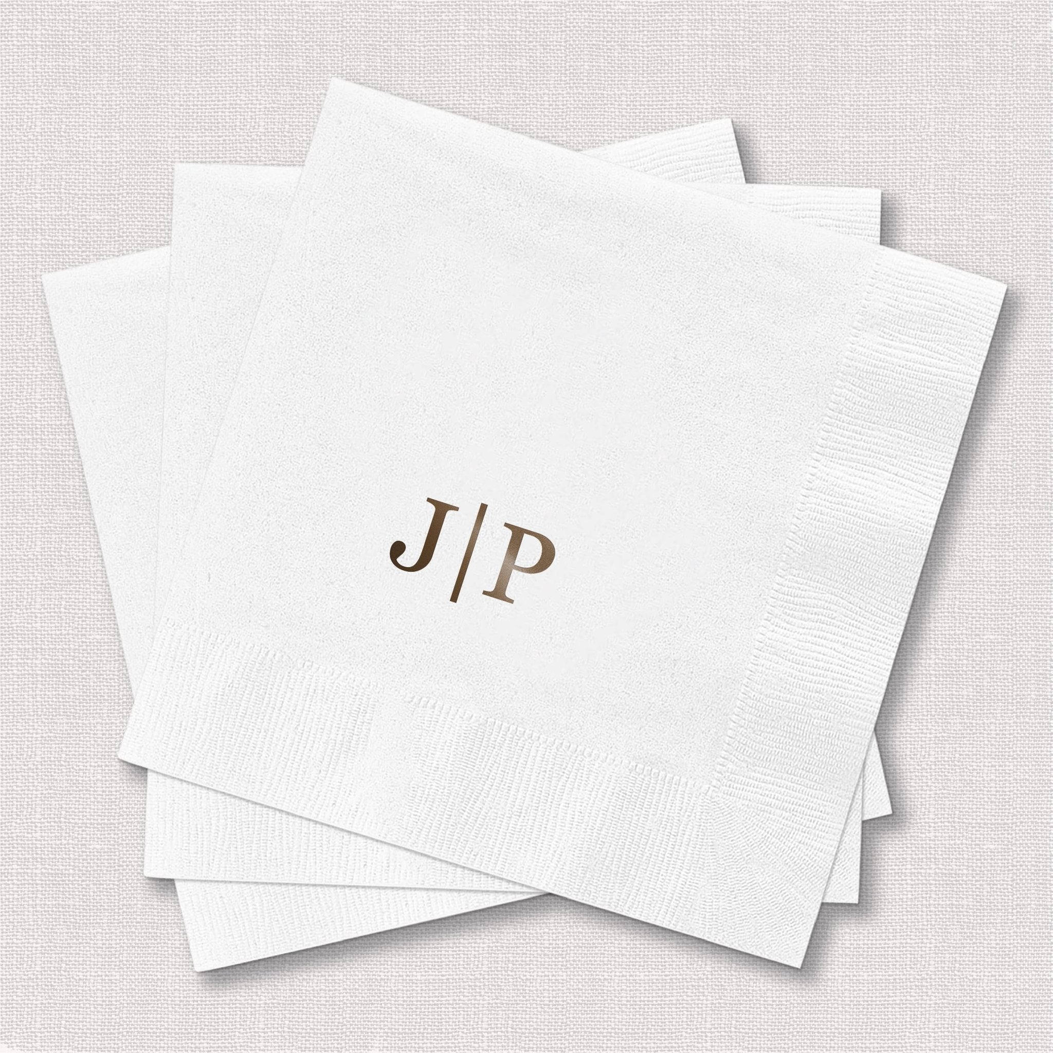 Stack of white foil-stamped napkins with gold monogram initials J and P separated by a line.