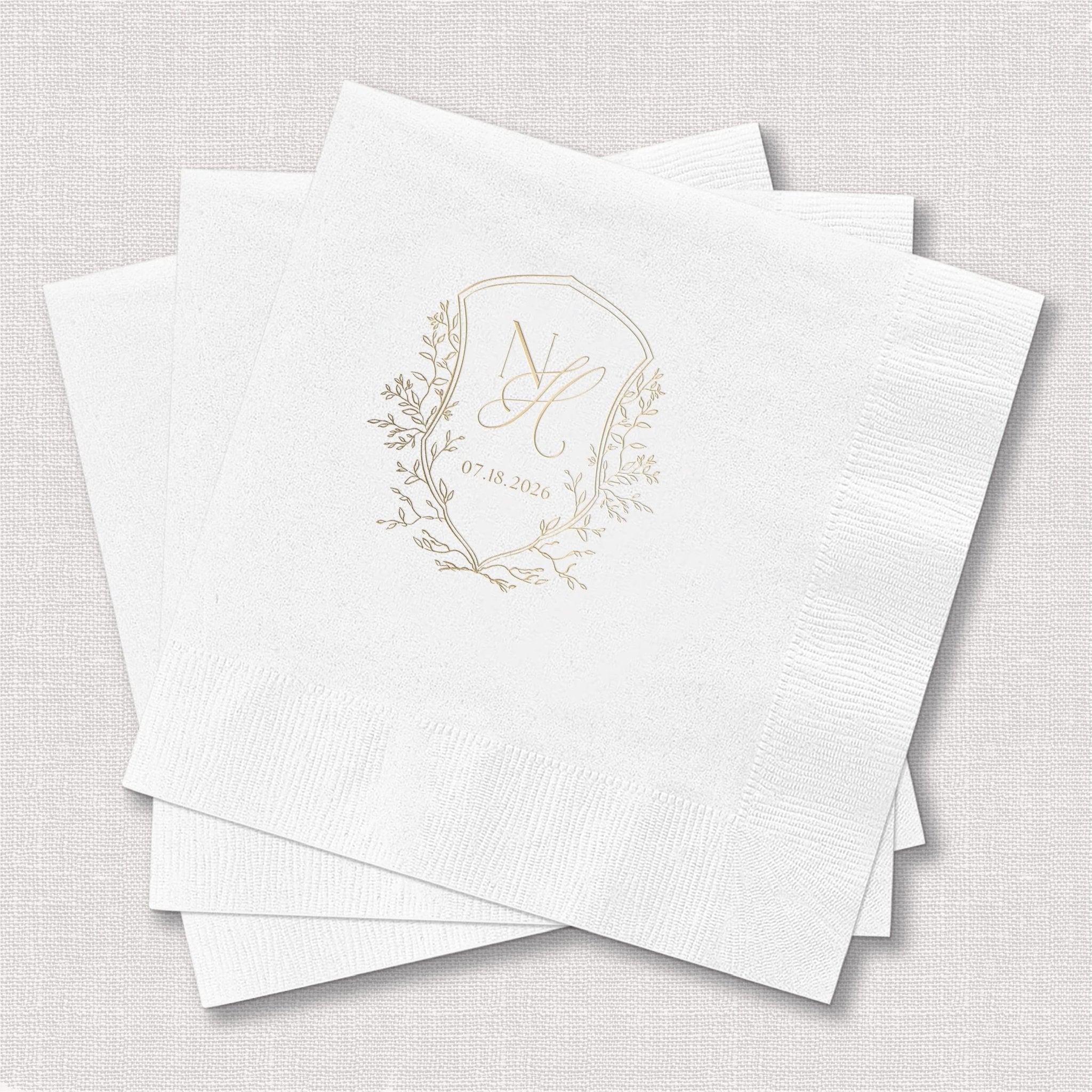 Stack of white beverage napkins with gold foil monogram and botanical wreath design