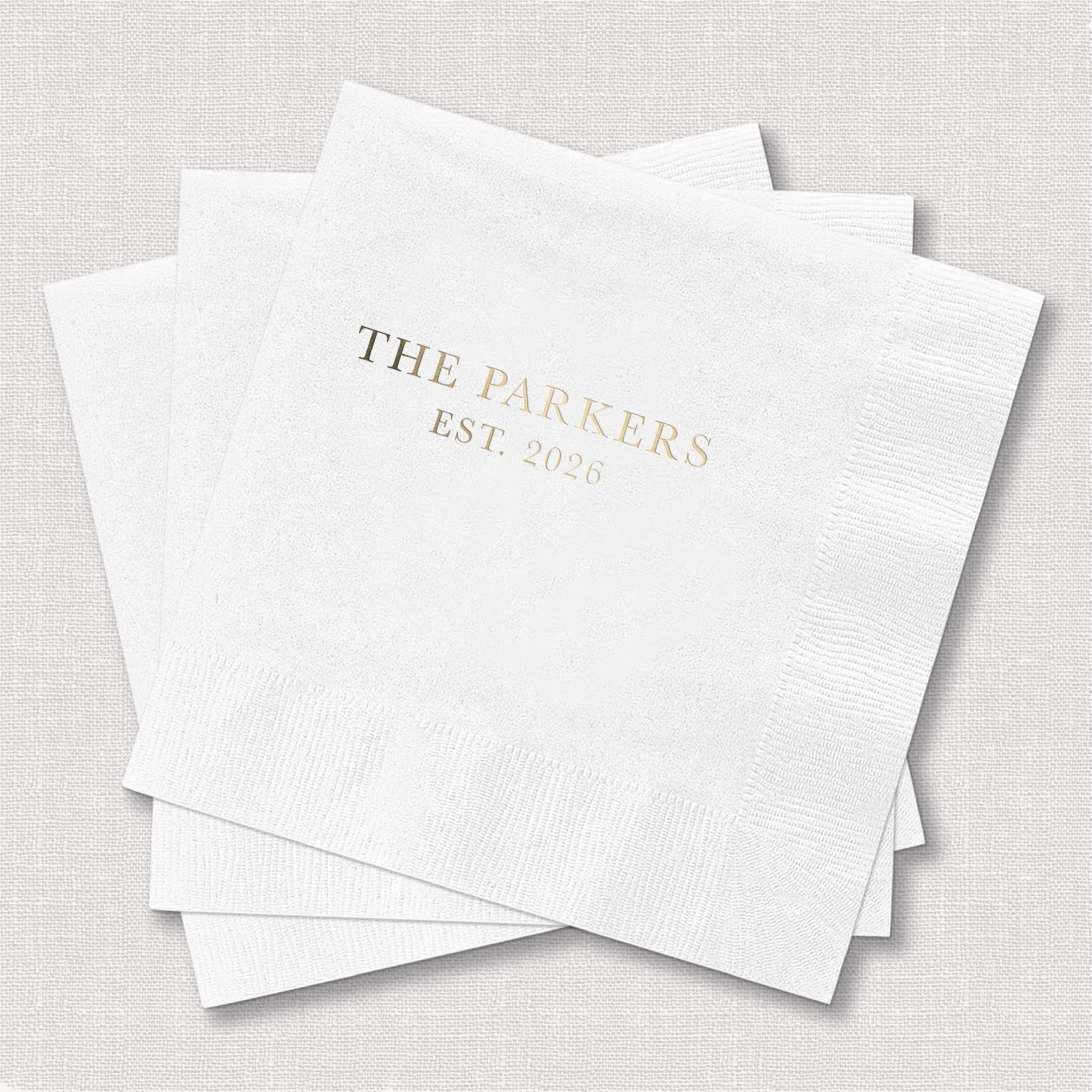 White cocktail napkins with gold foil stamped text reading "THE PARKERS EST 2025"