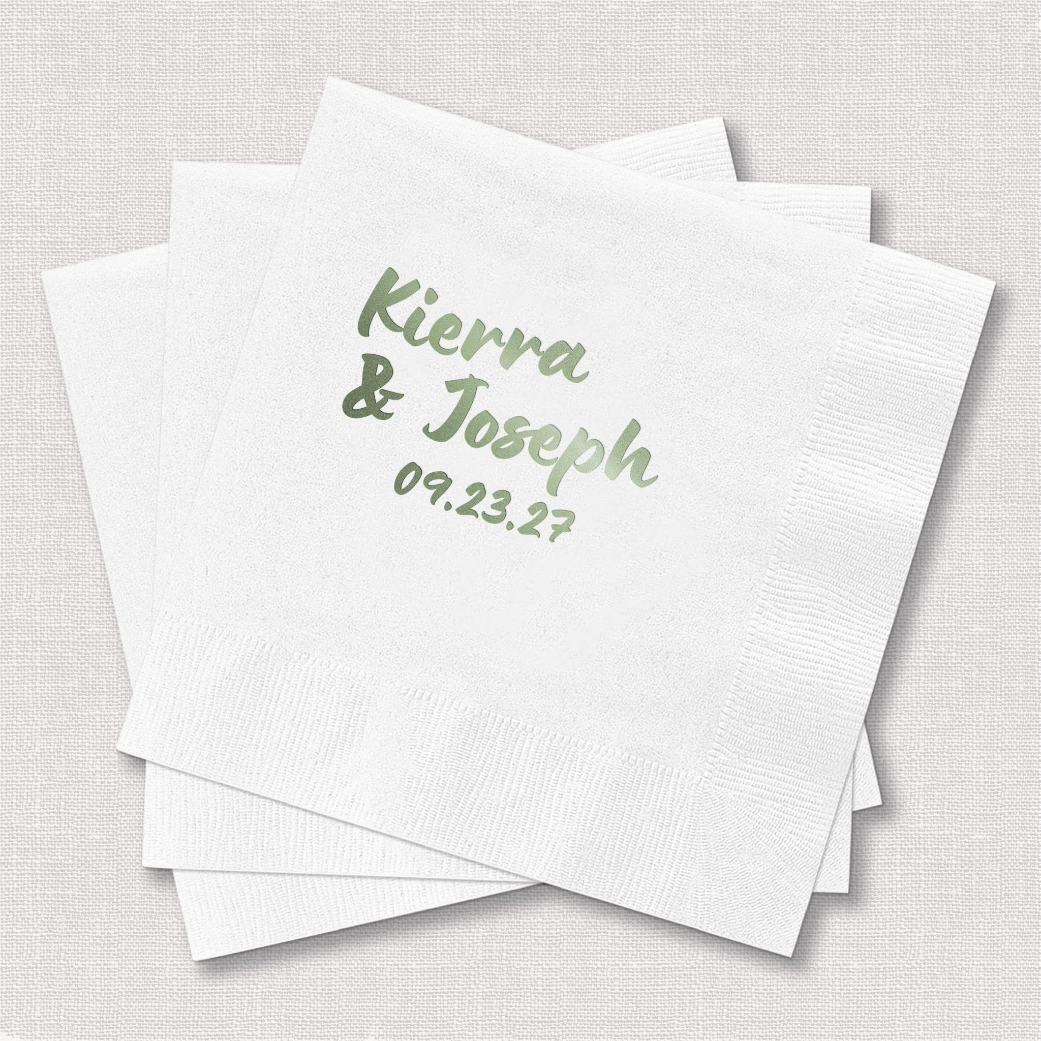White cocktail napkins with sage green foil-stamped names "Kierra & Joseph" and wedding date 09.23.27