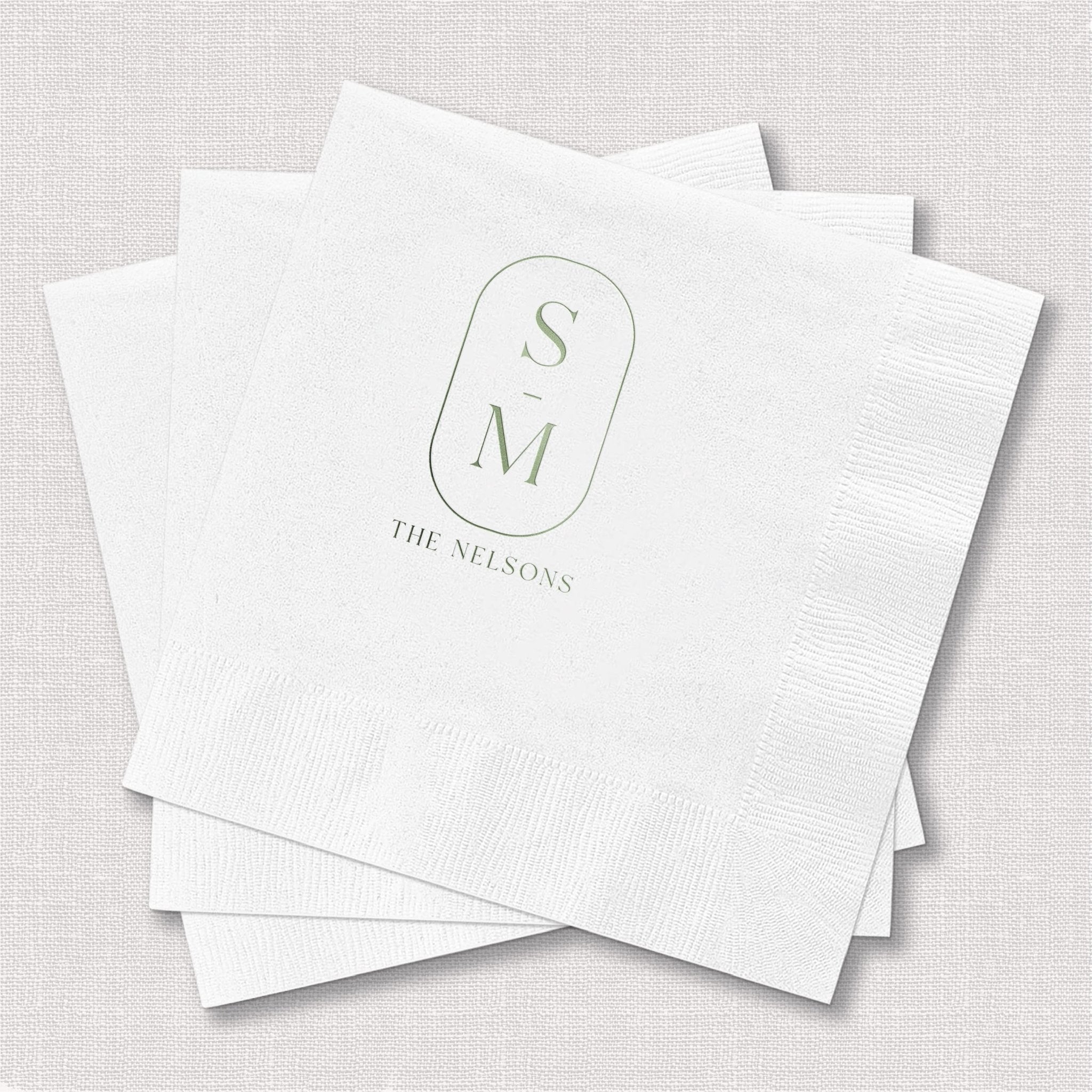 Stack of white beverage napkins with monogram SM and "THE NELSONS" text in gold foil stamping