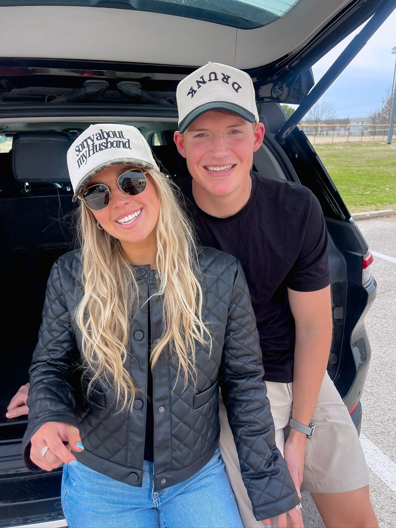Couple wearing matching vintage trucker hats that read "Sorry about my Husband" and "Sorry about my Wife" in a vehicle.