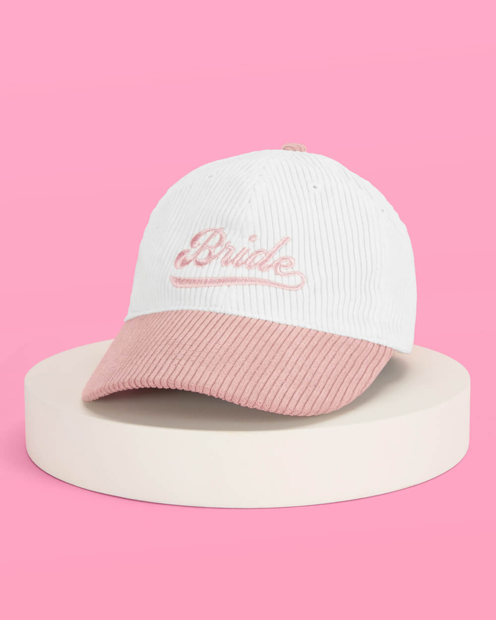 White and pink corduroy baseball cap with "Bride" embroidered on the crown against pink background