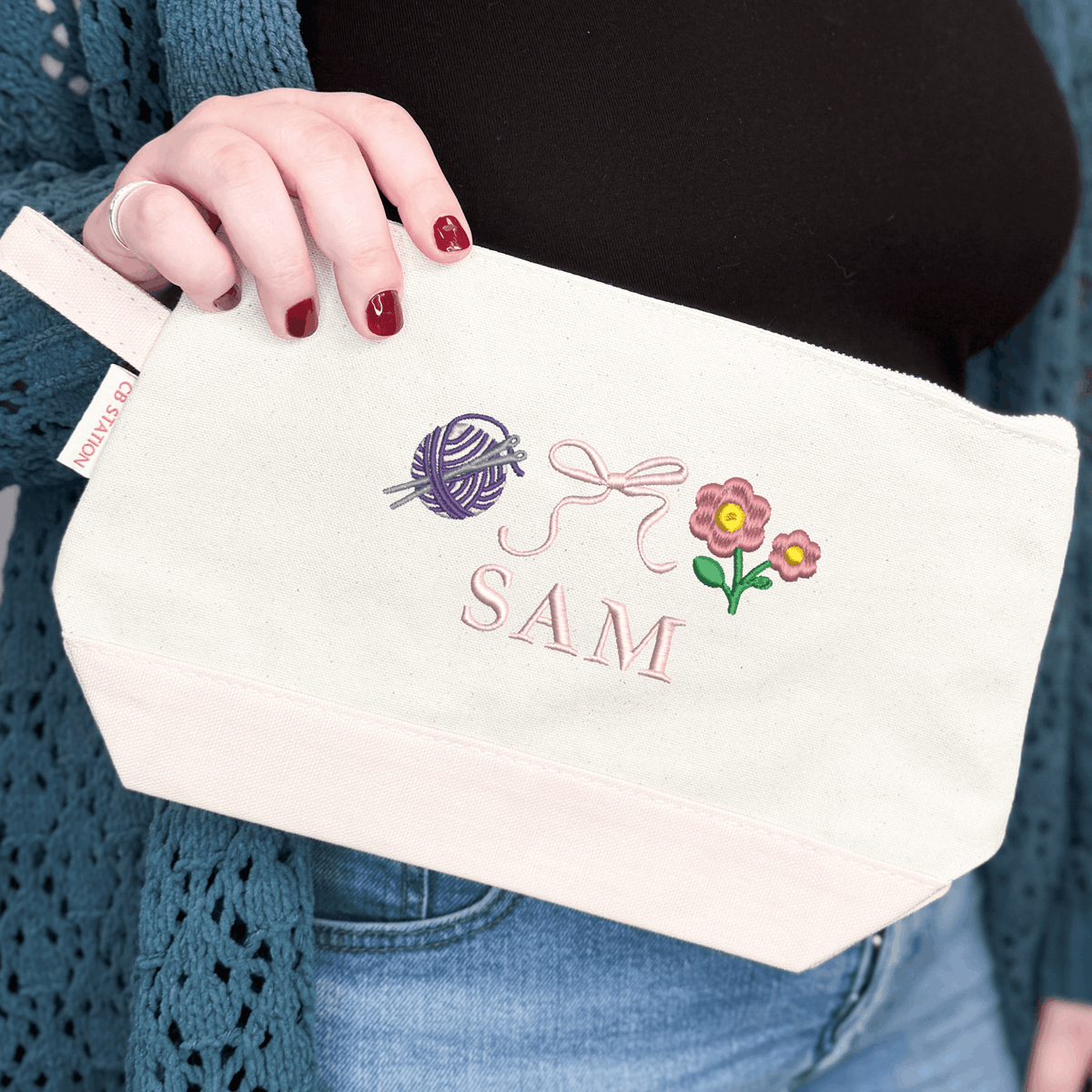 Natural canvas personalized makeup bag with embroidered yarn ball, bow and flower icons above the name SAM