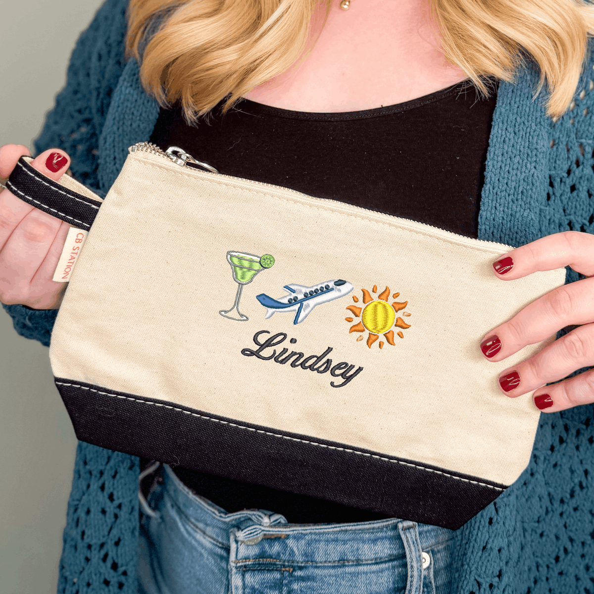 Personalized icon cosmetic bag with embroidered martini, airplane and sun icons and the name Lindsey in script, natural canvas with black trim