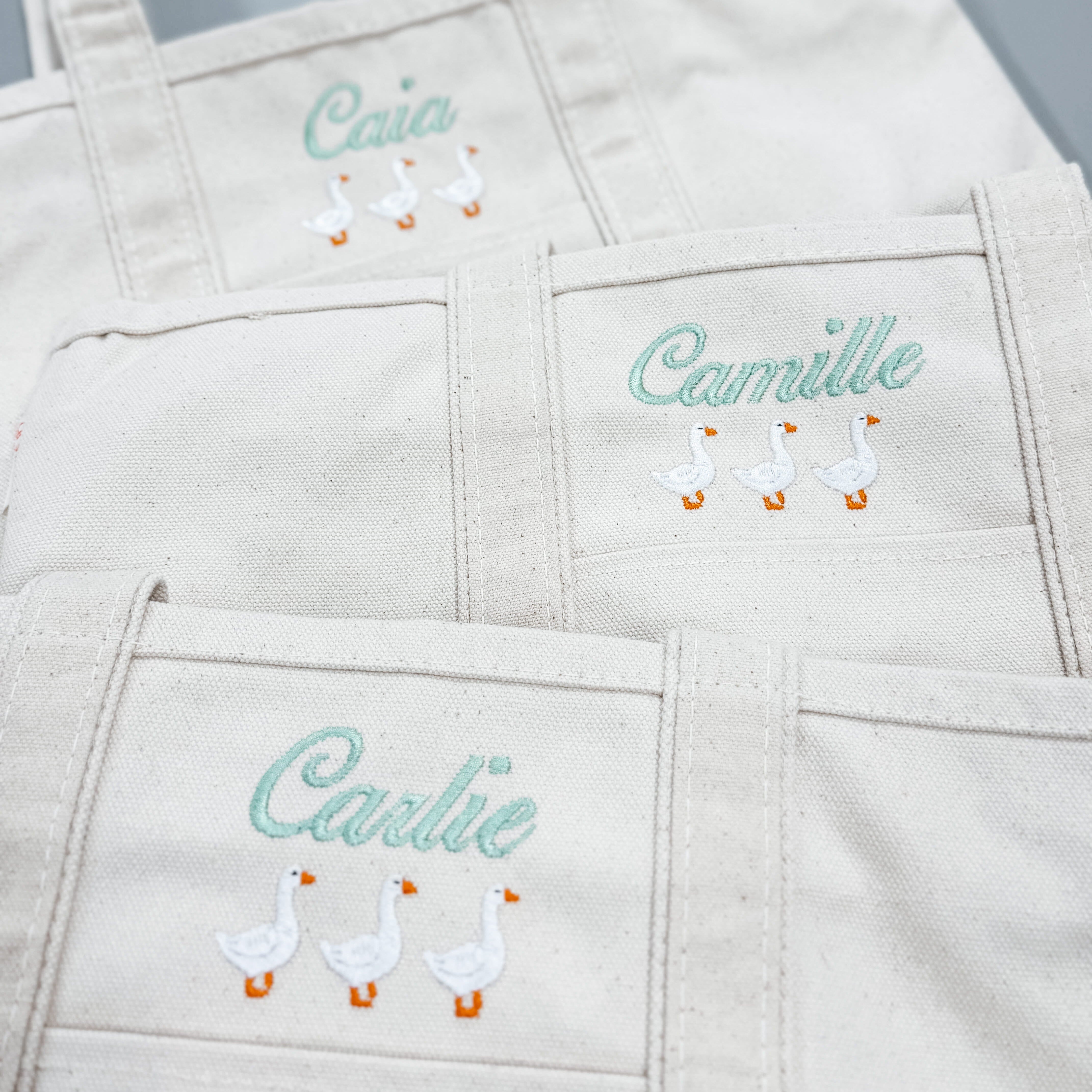 Three personalized embroidered goose canvas tote bags with custom names in mint green thread