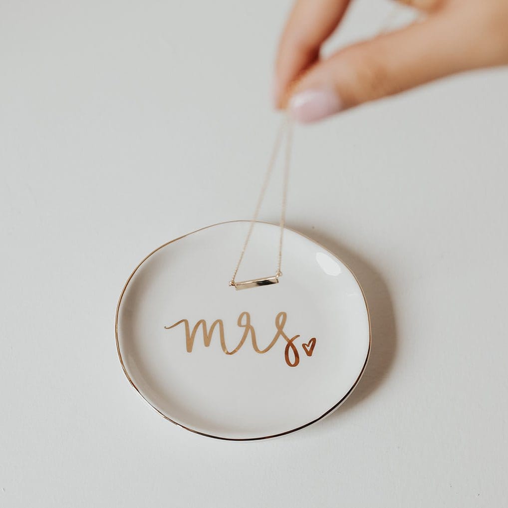 White ceramic jewelry dish with "mrs" in gold script and small heart detail, held by twine loop
