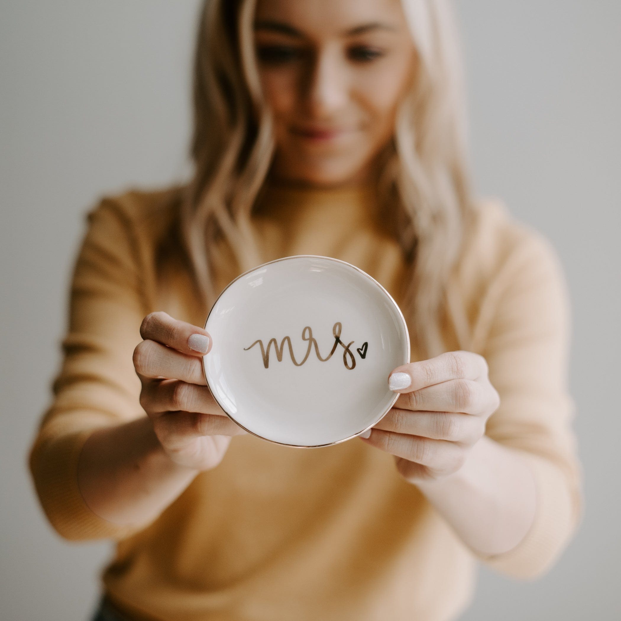 White ceramic dish with rose gold "mrs." script held by woman in beige sweater