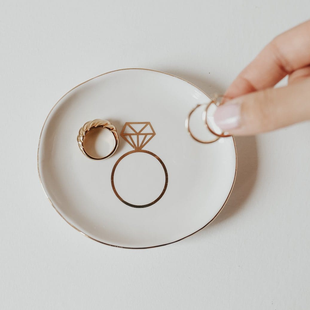 Cream ceramic jewelry dish with rose gold ring holders and diamond design, held by hand
