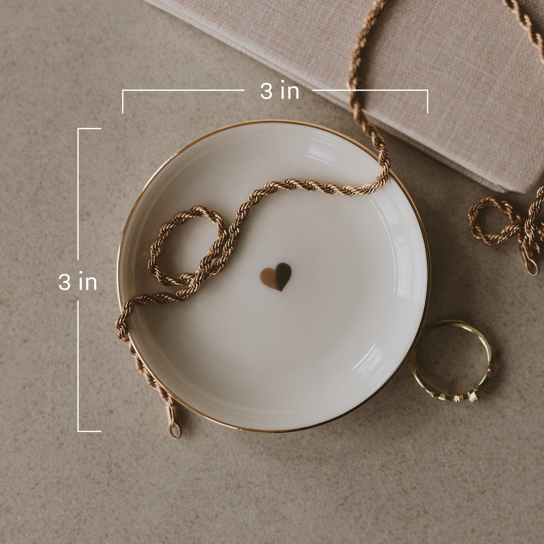 White ceramic dish with gold rim, small heart design in center, 3 inch size, styled with twine and rings.