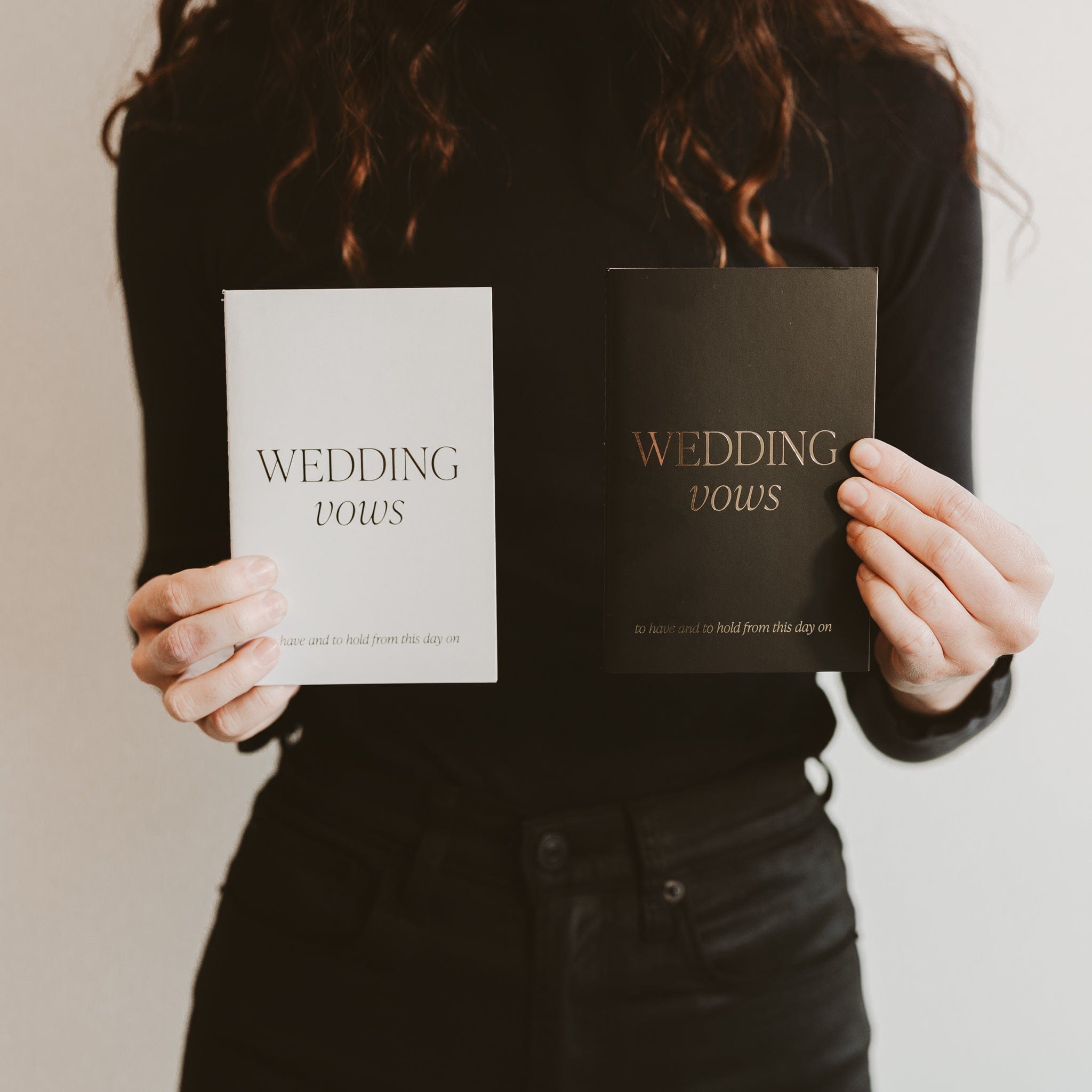 Woman holding white and black wedding vows journals with elegant gold text design