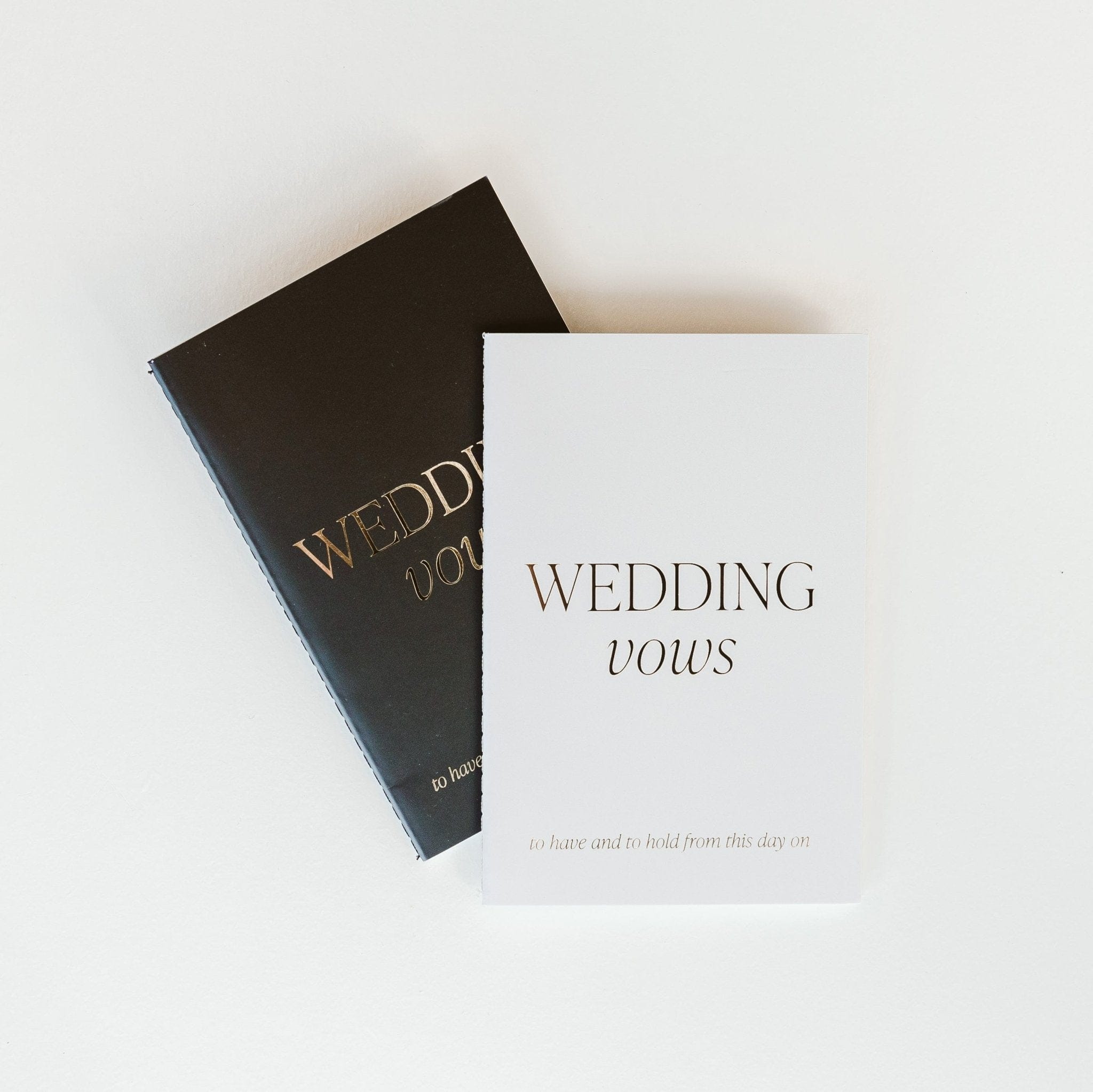 Black and cream wedding vows journals stacked together, featuring gold and black text on covers