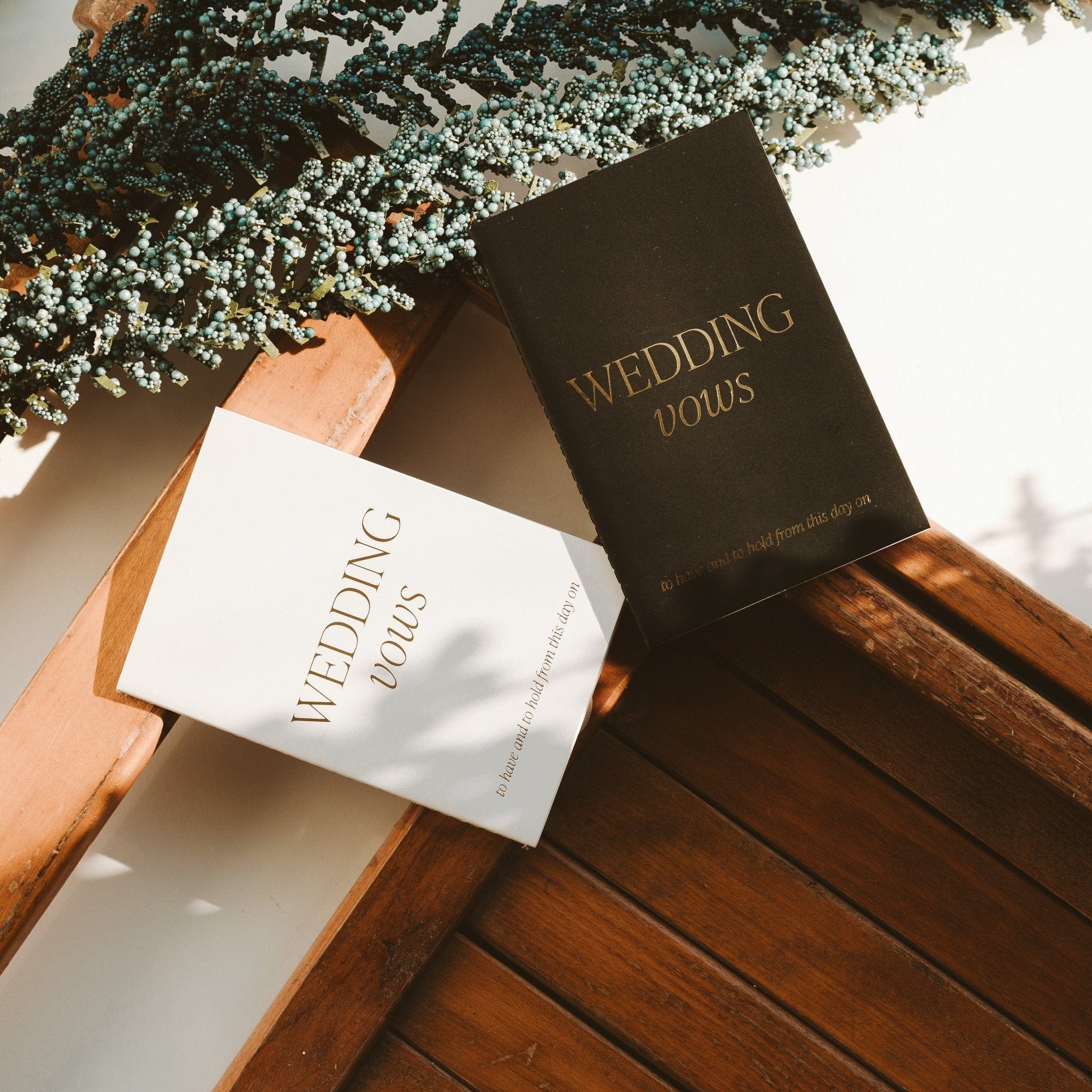 Black and white wedding vows journals with gold text on wooden surface and baby's breath flowers