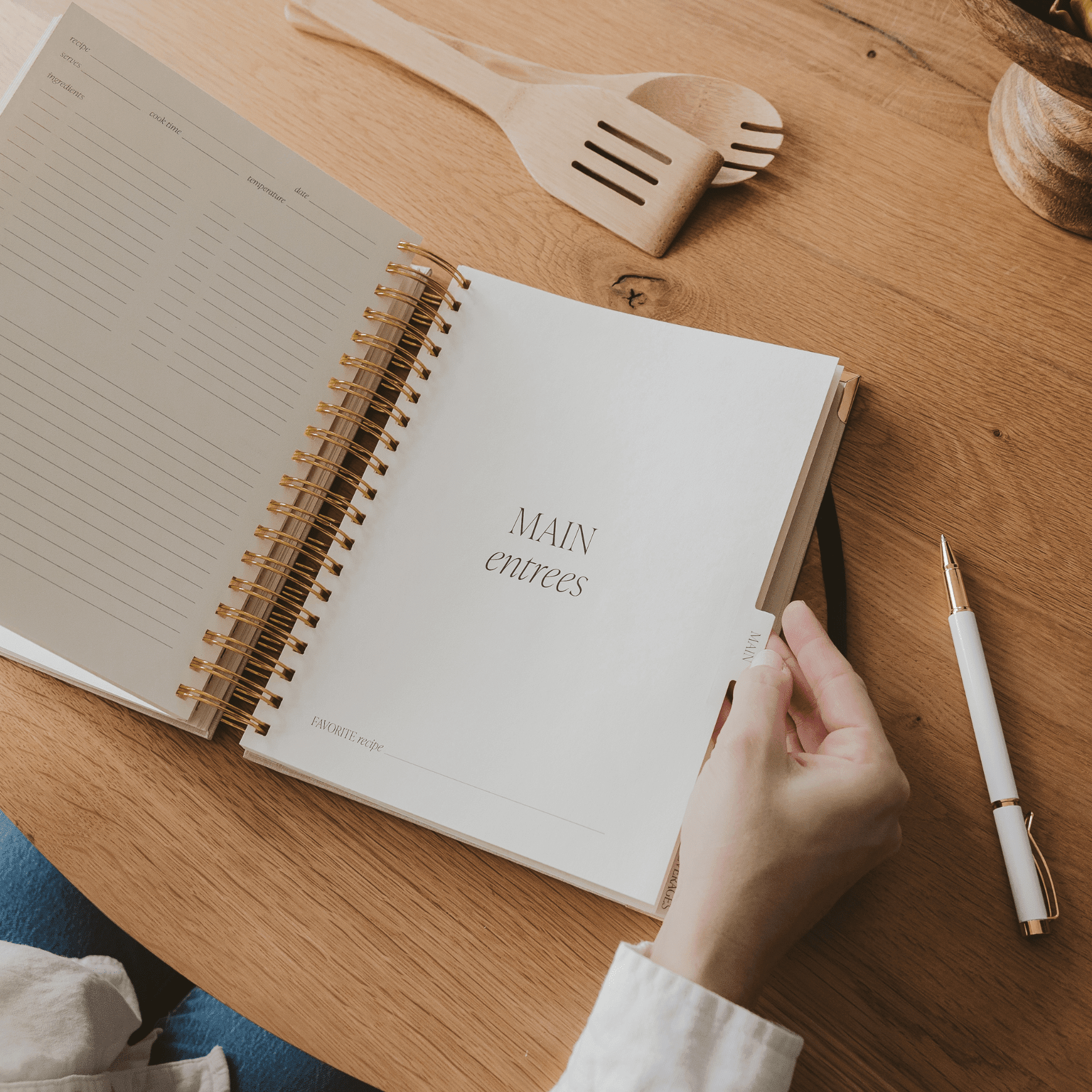 Open recipe book with "MAIN COURSES" text on white page, spiral binding, wooden desk setting.