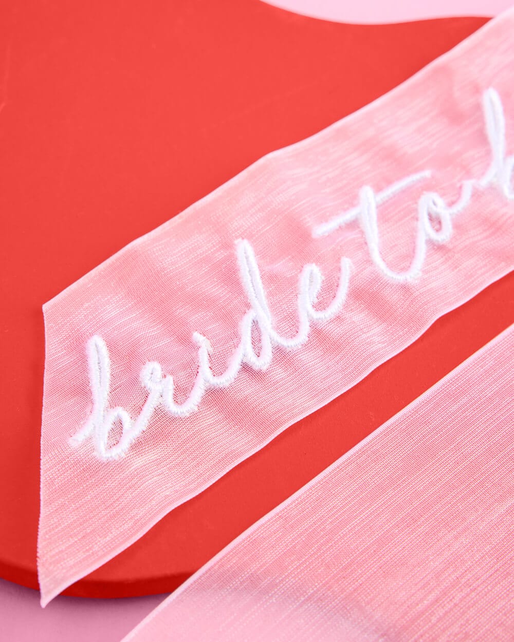 Pink fabric bow with white embroidered "Bride to Be" text on red and pink background