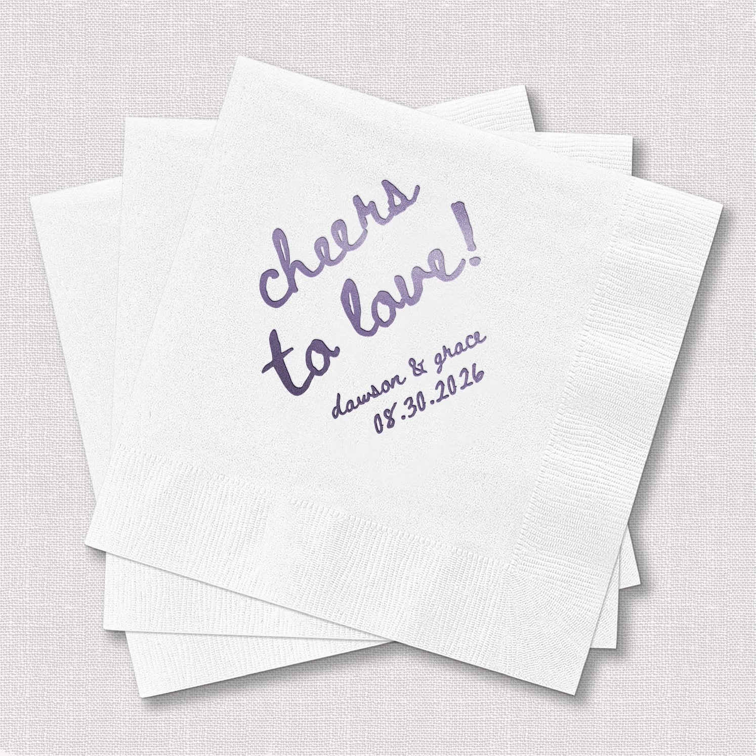 Stack of personalized white cocktail napkins with "Cheers to Love" script design printed in purple