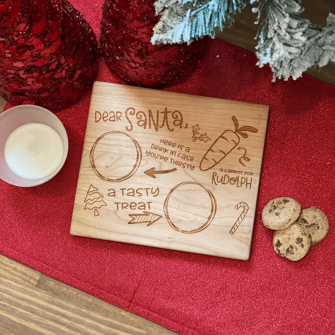 Wooden engraved cherry board with "Dear Santa" message and circular compartments for treats, surrounded by holiday decorations and cookies.