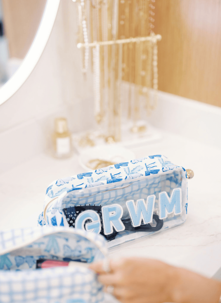 Clear makeup bag with blue bow pattern and "GRWM" text in white lettering, sitting on bathroom vanity