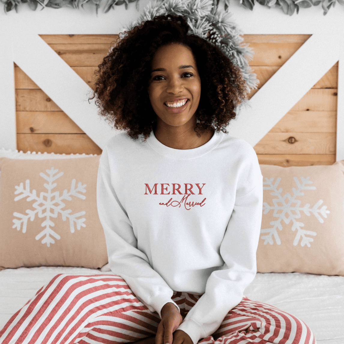 Woman wearing white crewneck sweatshirt with "Merry And Married" text in red, styled with red striped pajama pants.