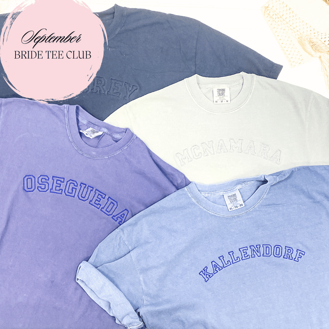 Three stacked t-shirts in purple, cream, and light blue with embroidered text including "Osegueda" and "Hallendorf," featuring a "September Bride Tee Club" circular logo.