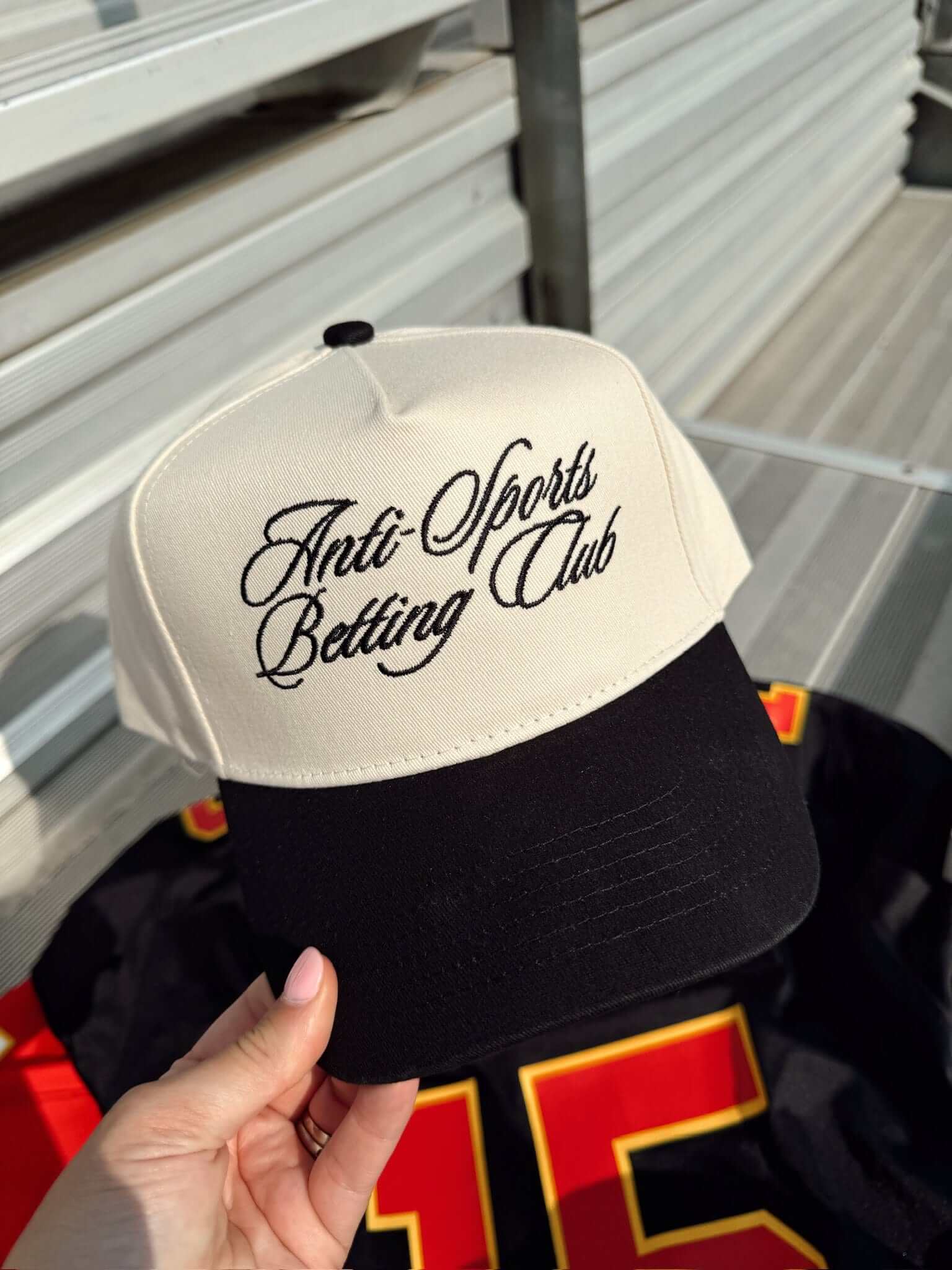 White and black vintage trucker hat with "Anti Sports Betting Club" script embroidery on the front panel and orange accent details.