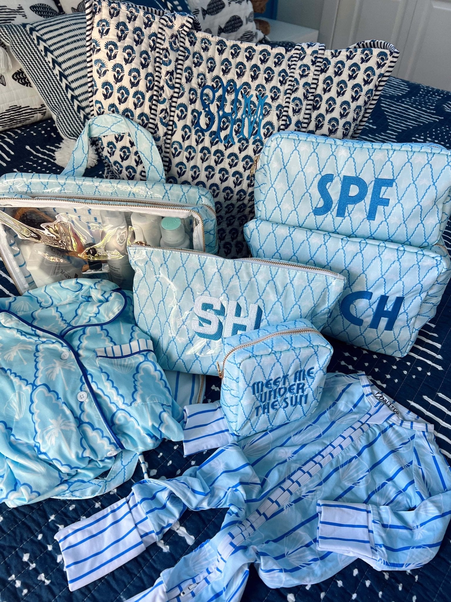 Blue quilted makeup bag with SPF text and geometric pattern, displayed with coordinating blue patterned accessories and bedding