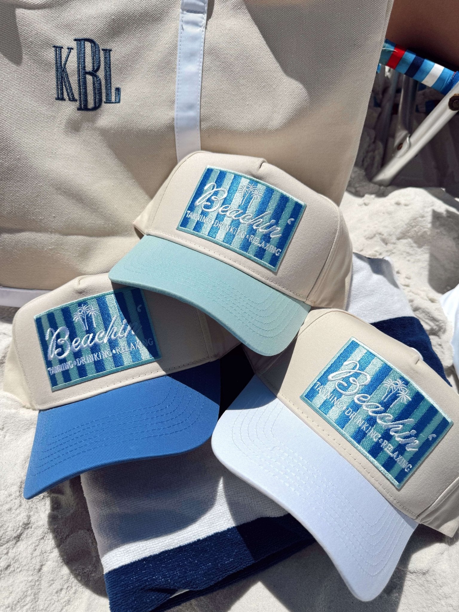 Three vintage-style trucker hats with "Beachin'" text and blue striped design on front panels, in light blue, white, and navy colorways