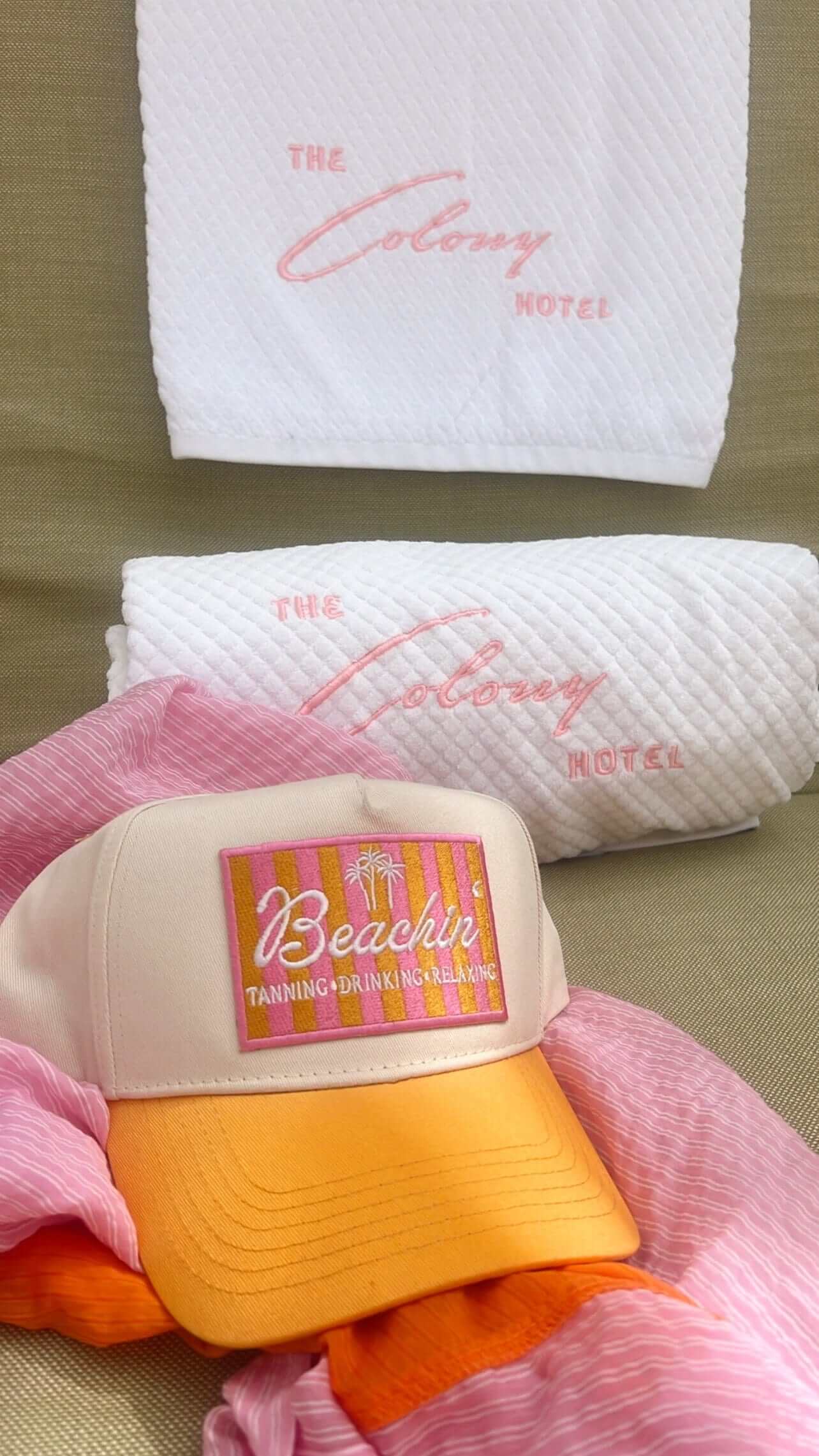 Cream and yellow vintage trucker hat with "Beachin" patch, displayed with pink personalized napkins featuring "The Colony Hotel" text.