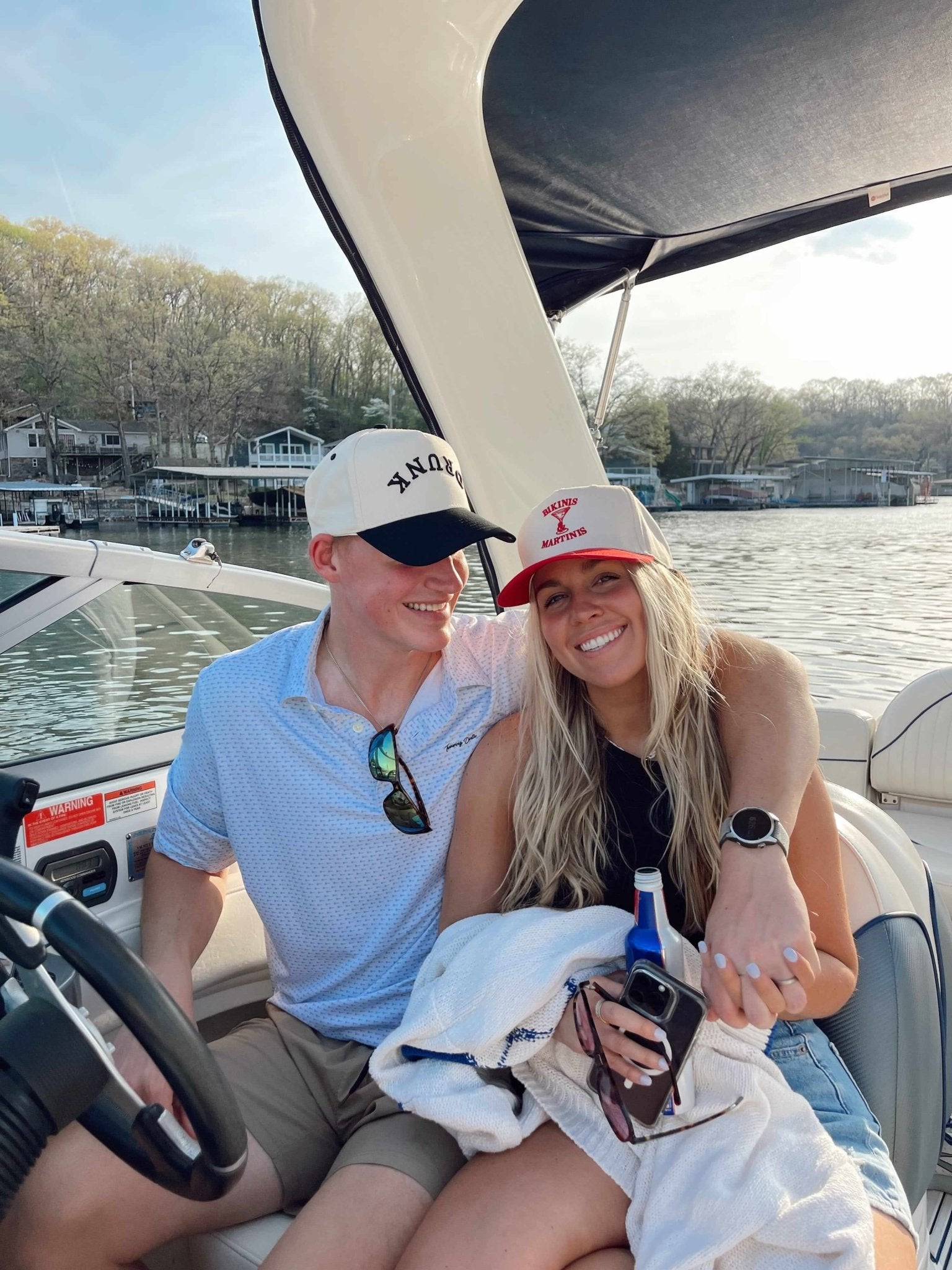 White trucker hat with black mesh back and "DRUNK" text printed on front panel, worn by man on boat.
