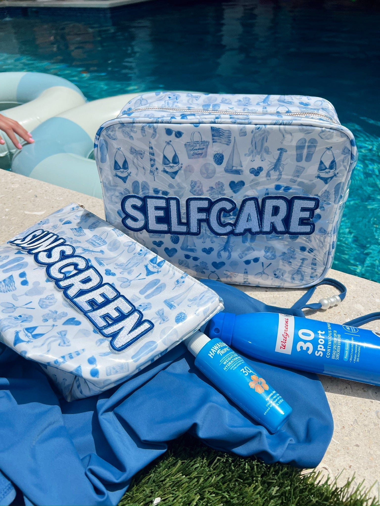 Clear cosmetic bag with blue Americana pattern and "SELFCARE" text, displayed poolside with coordinating pouches