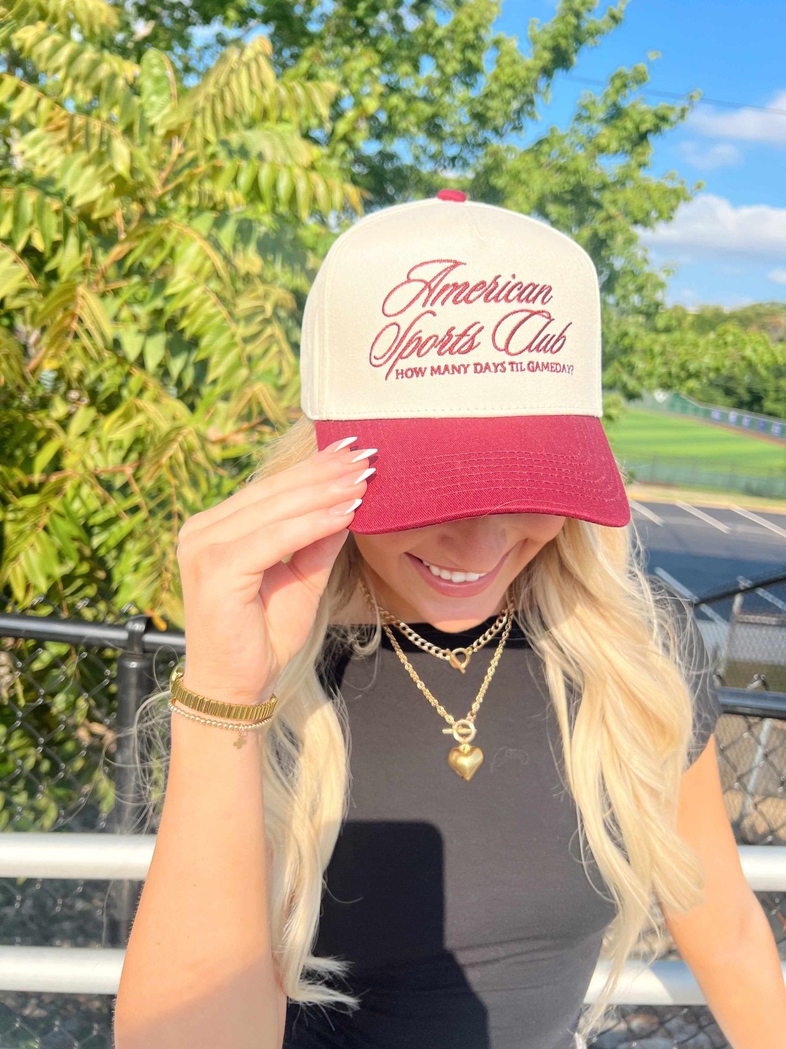 Cream and pink trucker hat with American Sports Club vintage script design, worn by woman outdoors.