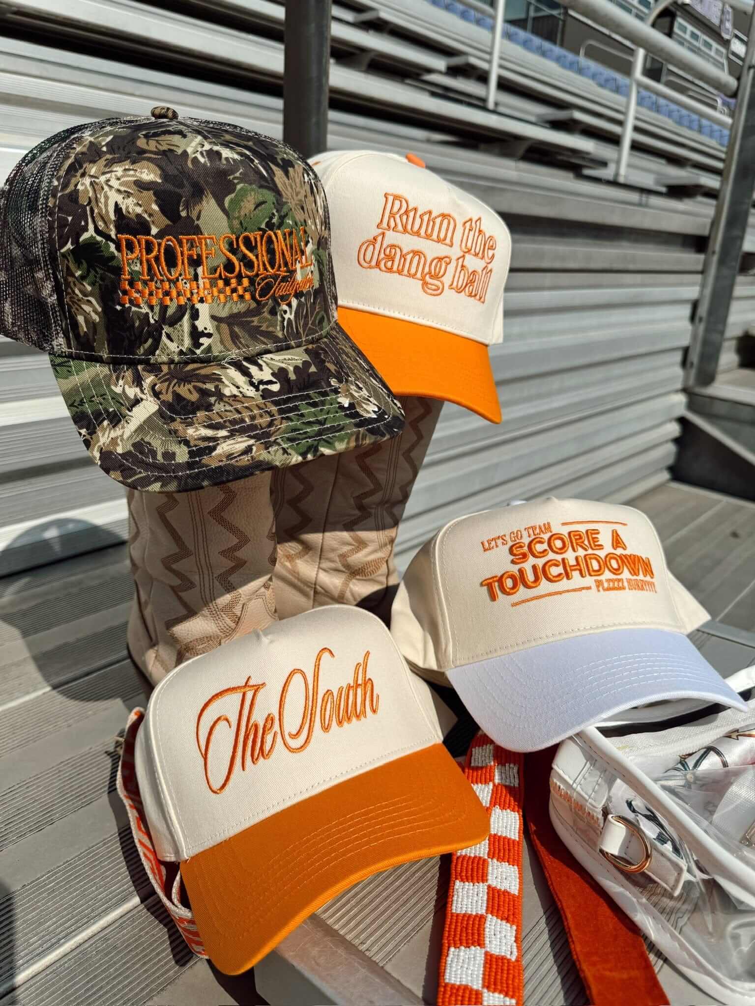 Camo and orange trucker hats stacked together, featuring "The Oath" and other text designs in orange lettering on white and orange panels.