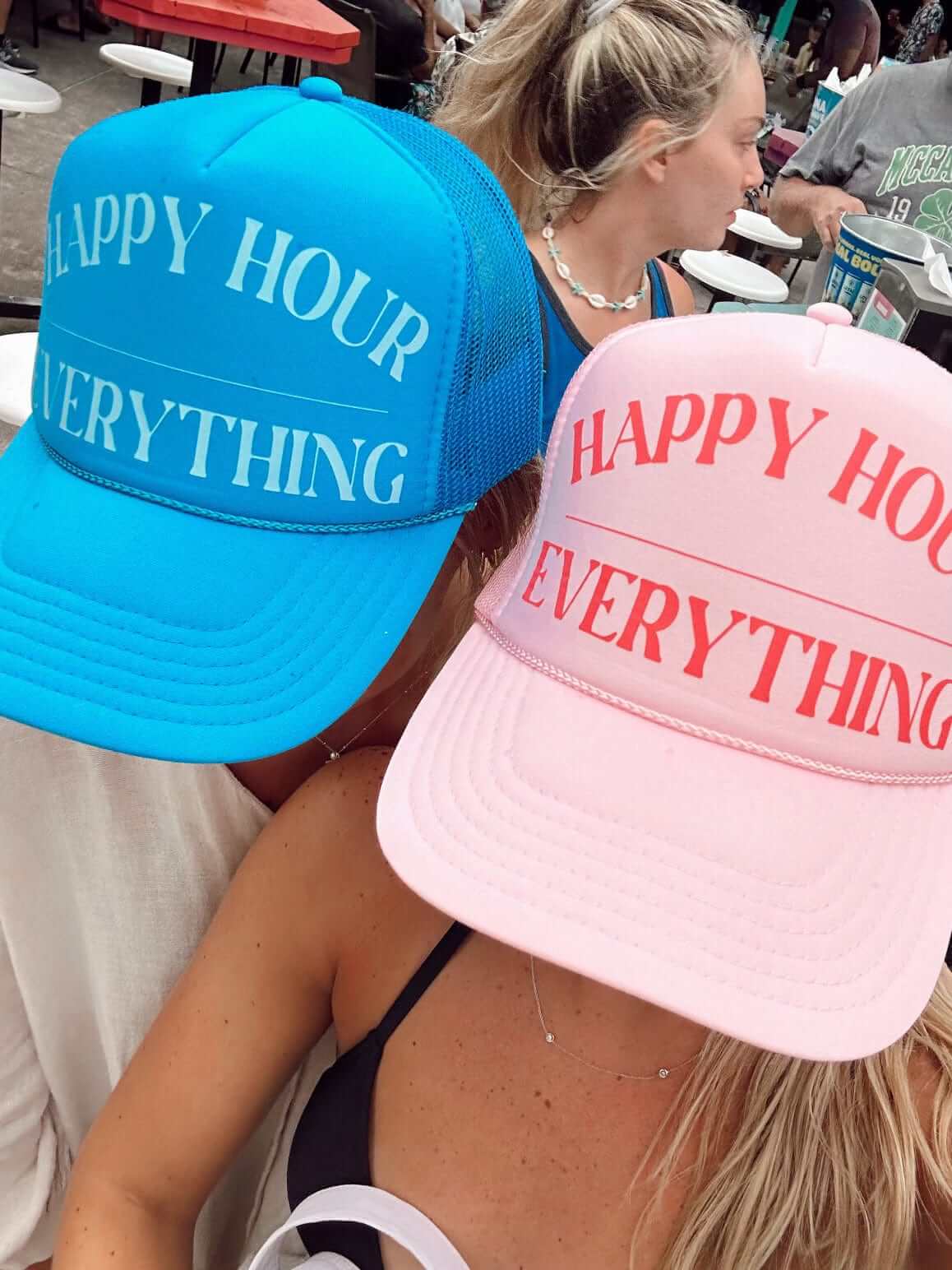Blue and pink mesh trucker hats with "Happy Hour Everything" text printed on the front panels