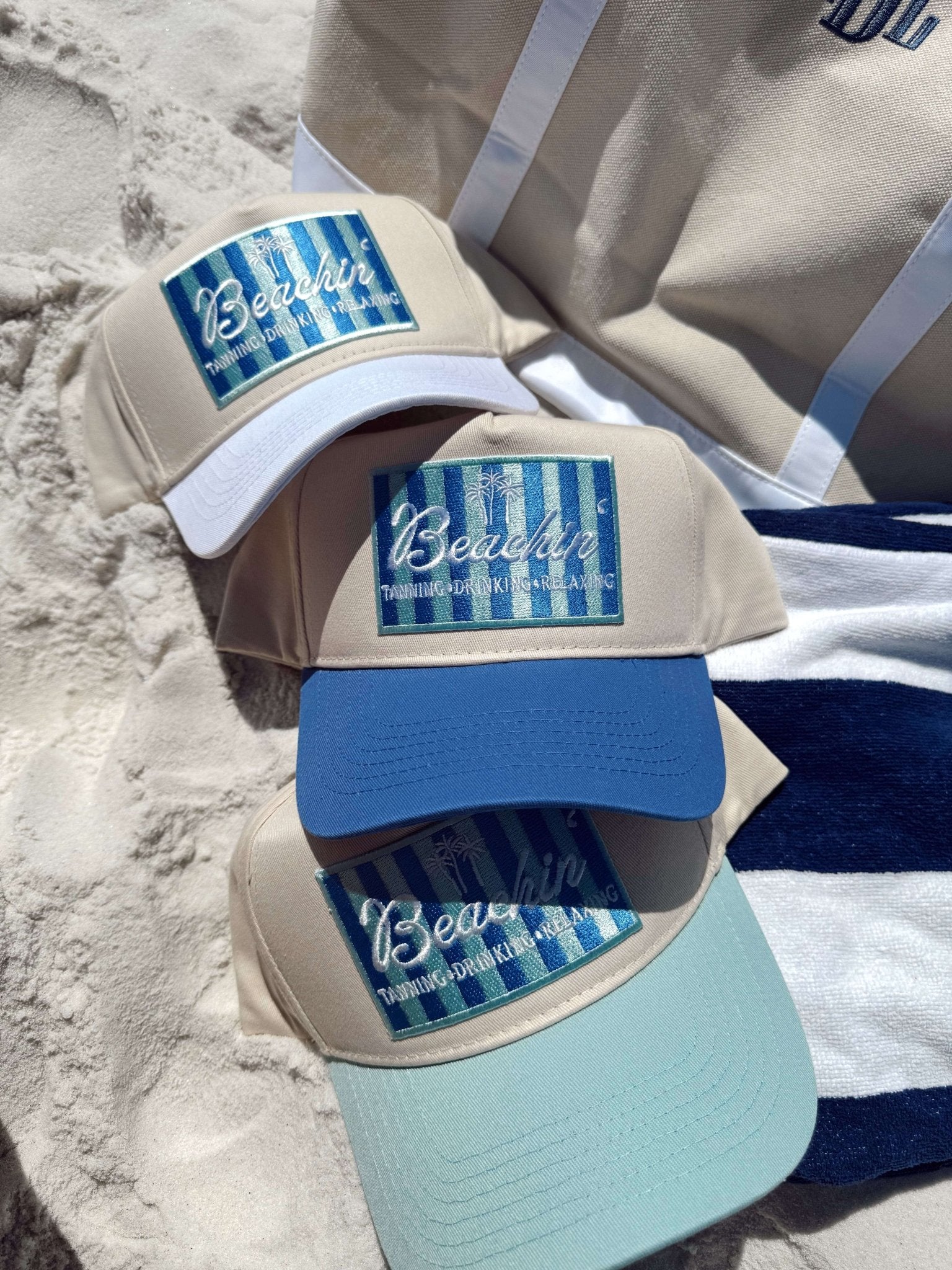 Stack of three vintage trucker hats with "Beachin'" script logo, featuring white, blue, and light turquoise panels on sandy beach.