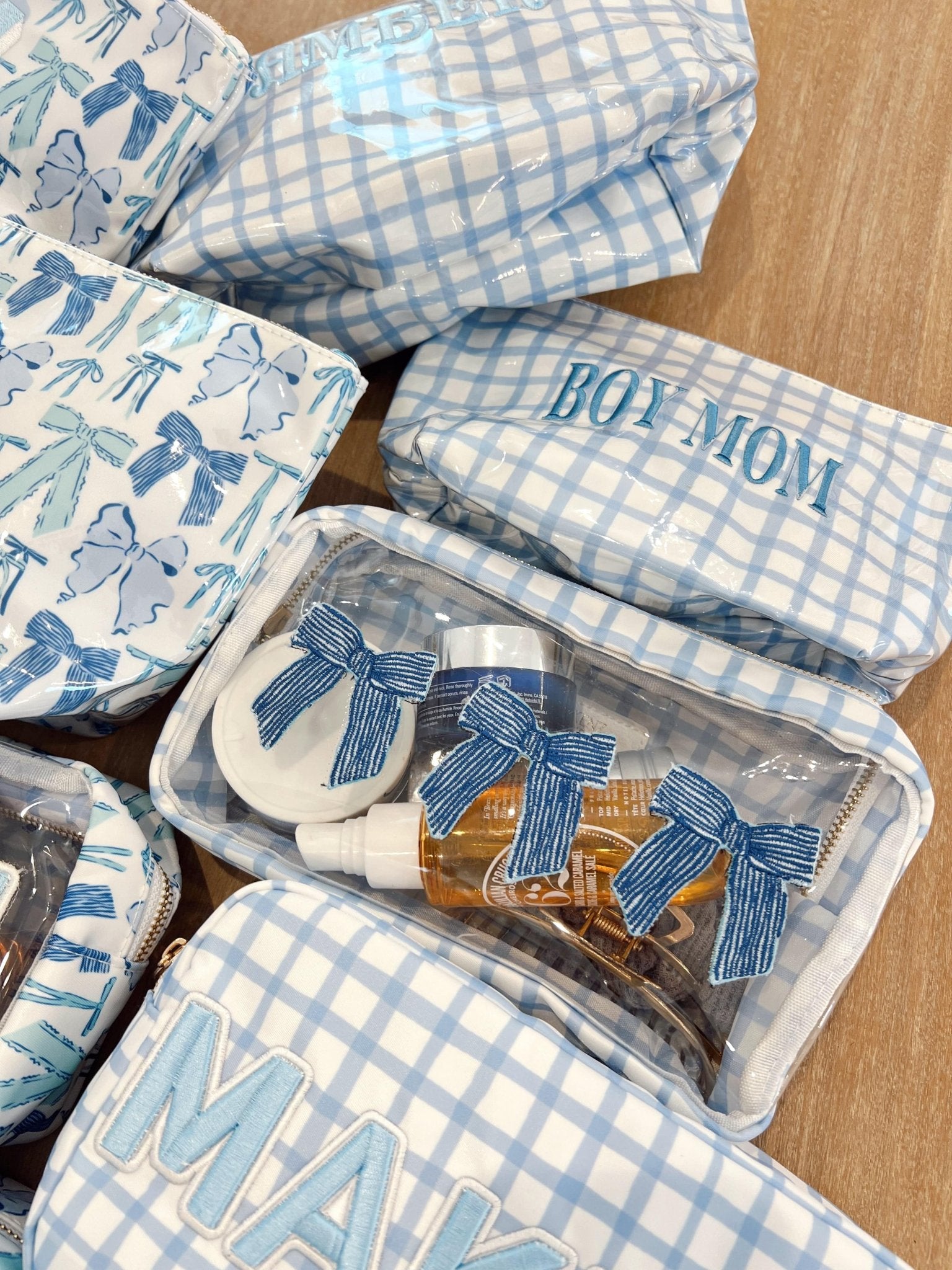 Blue gingham makeup bag with "HOT MOM" text, displayed with coordinating bow-printed pouches and accessories.
