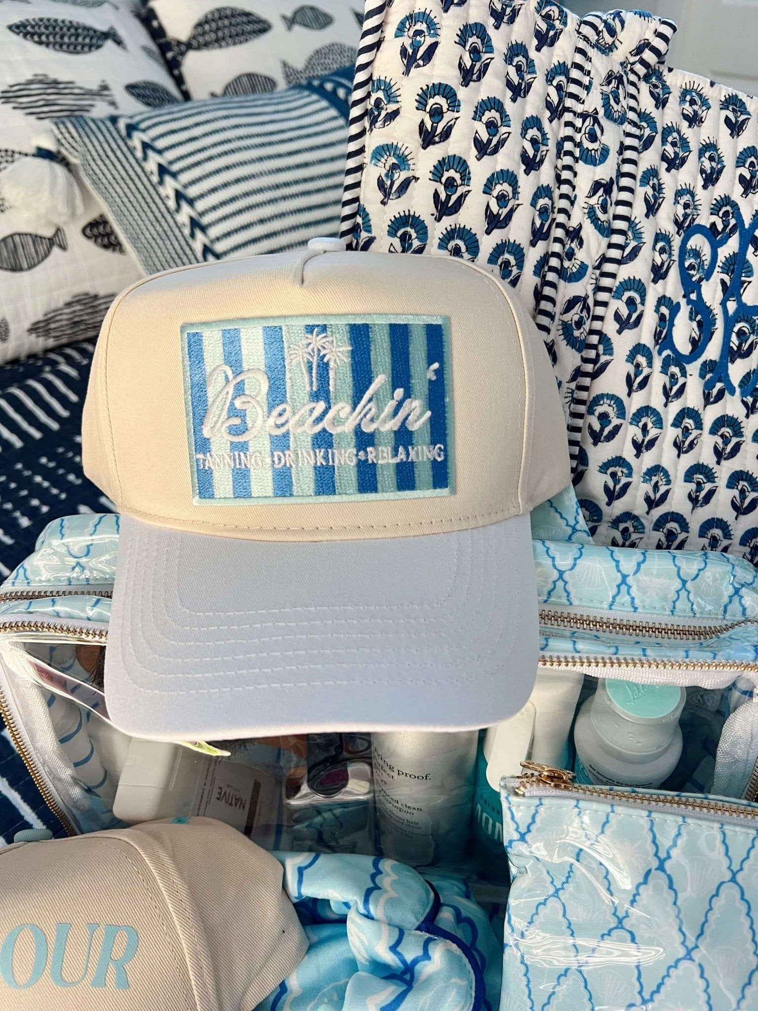 White and blue vintage trucker hat with striped mesh panel and coastal-themed design, displayed with coordinating beach-patterned drinkware and textiles.