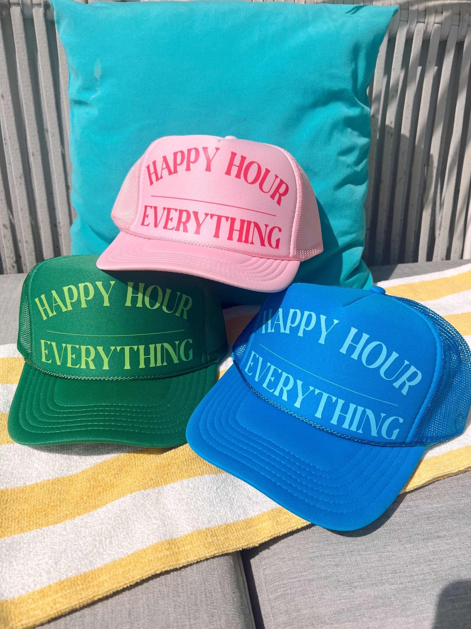 Three trucker hats in pink, green, and blue with "Happy Hour Everything" text embroidered on the front.