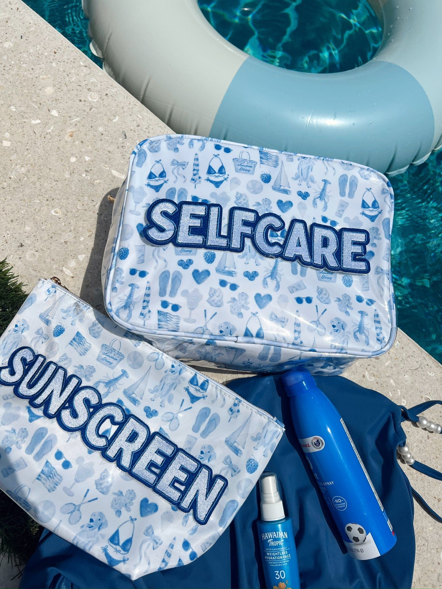 Blue and white patterned makeup bag with "SELFCARE" text, displayed poolside with sunscreen and beach items.