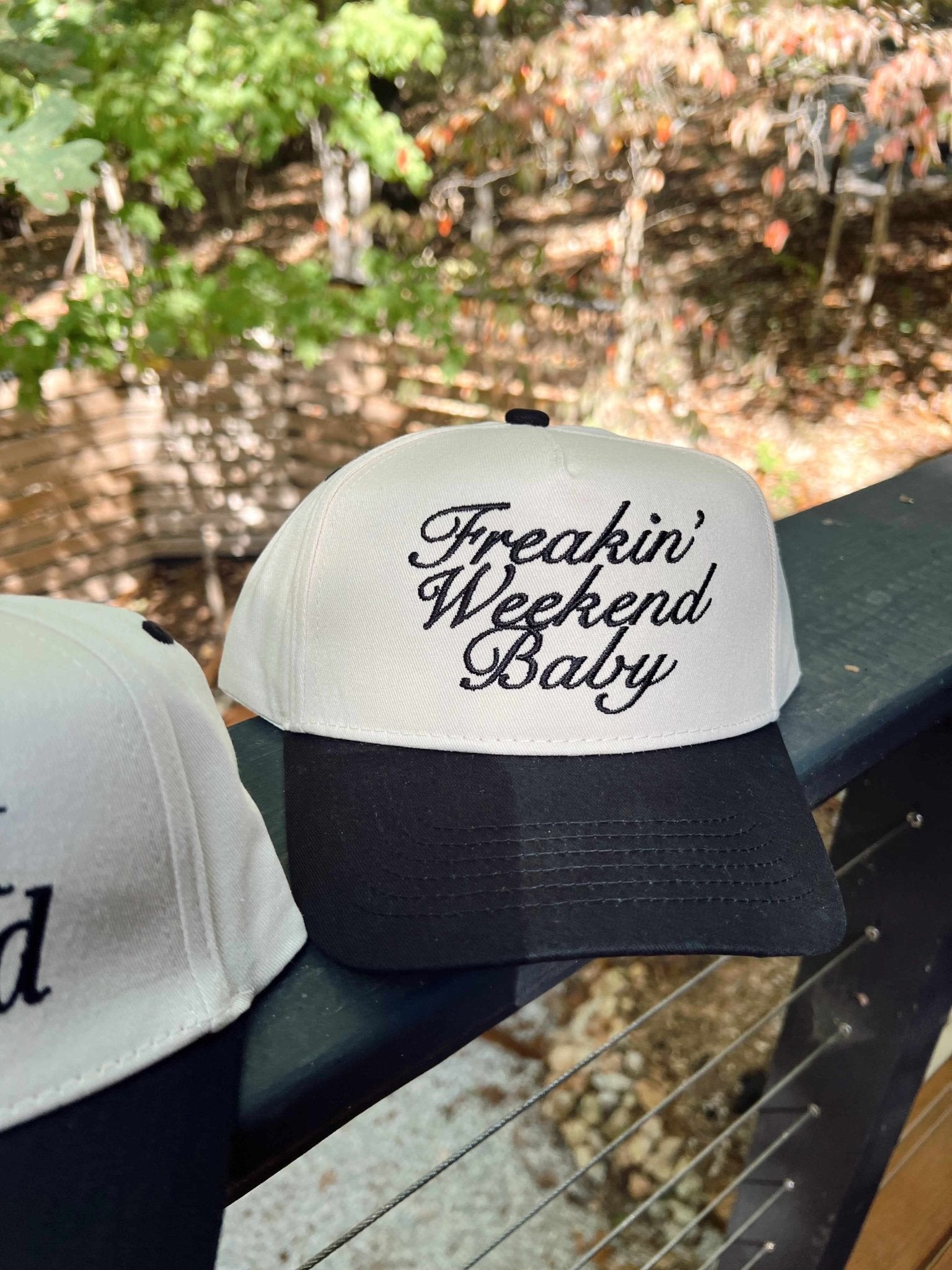 White and black vintage trucker hat with "Freakin' Weekend Baby" text embroidered on the front panel.